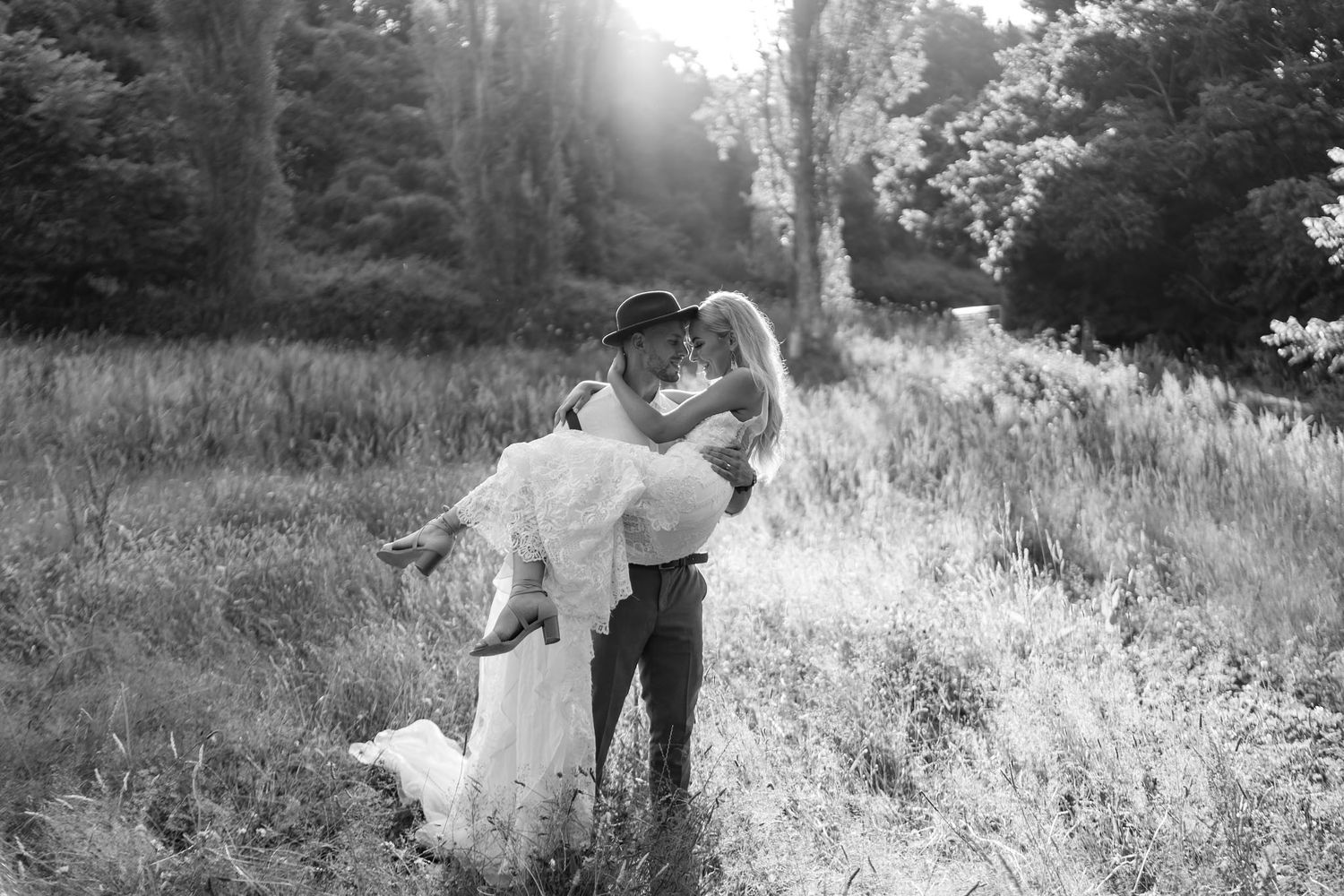Couple in rustic field embracing during golden hour photography session in tall grass meadow.