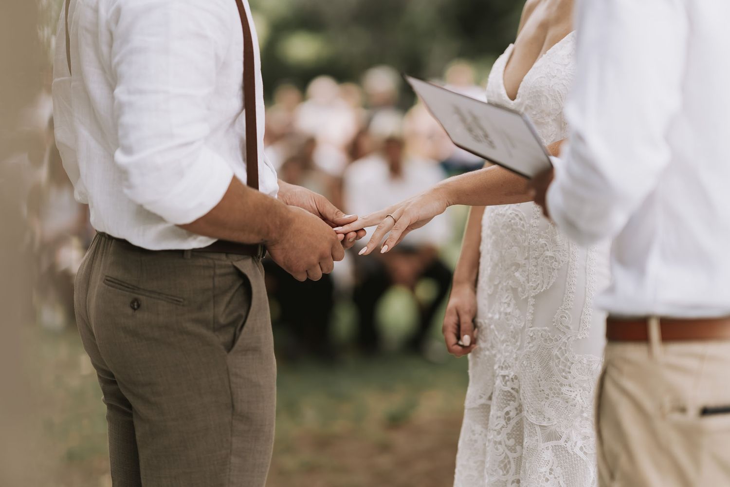 Couple exchanging vows during outdoor wedding ceremony with romantic blurred garden background and sun rays.