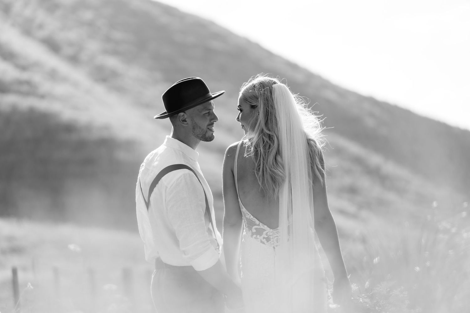 A couple in wedding attire share an intimate moment against a mountainous background in black and white.
