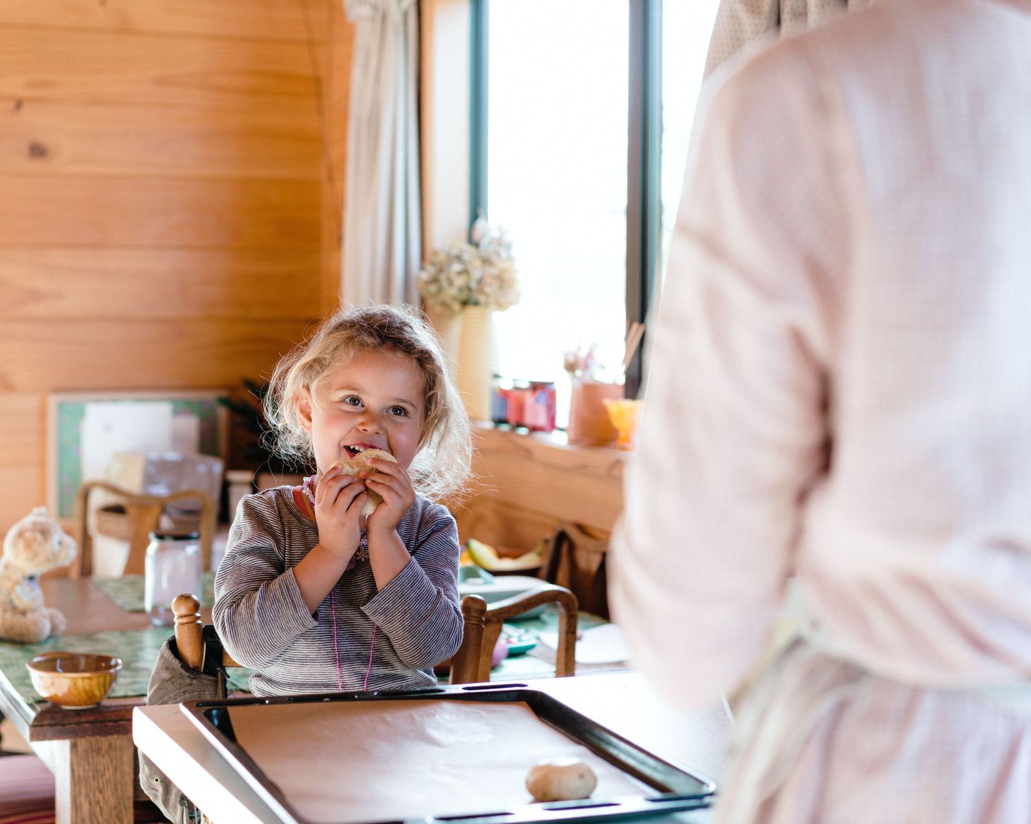 Young child wearing blue sweater stands at wooden counter while looking at food on a baking sheet.