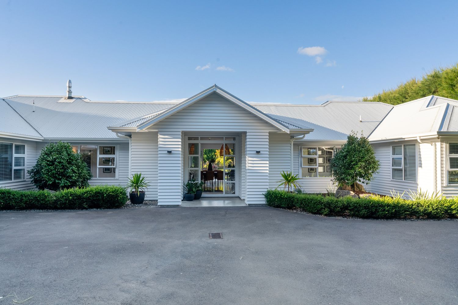 White single-story building exterior with front entrance and landscaped garden beds.