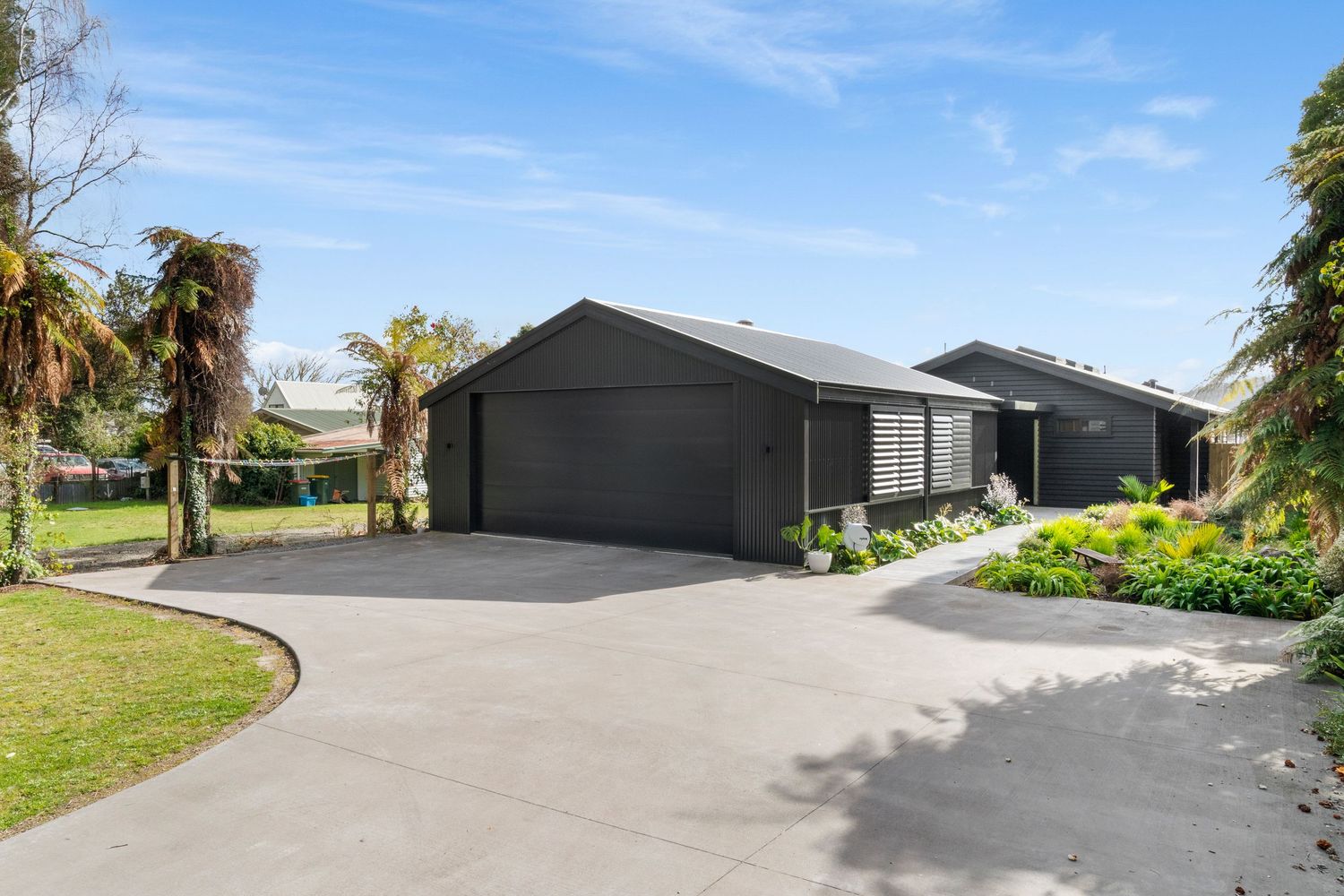 Modern black houses with garage doors line a curved driveway under blue skies in a residential development.