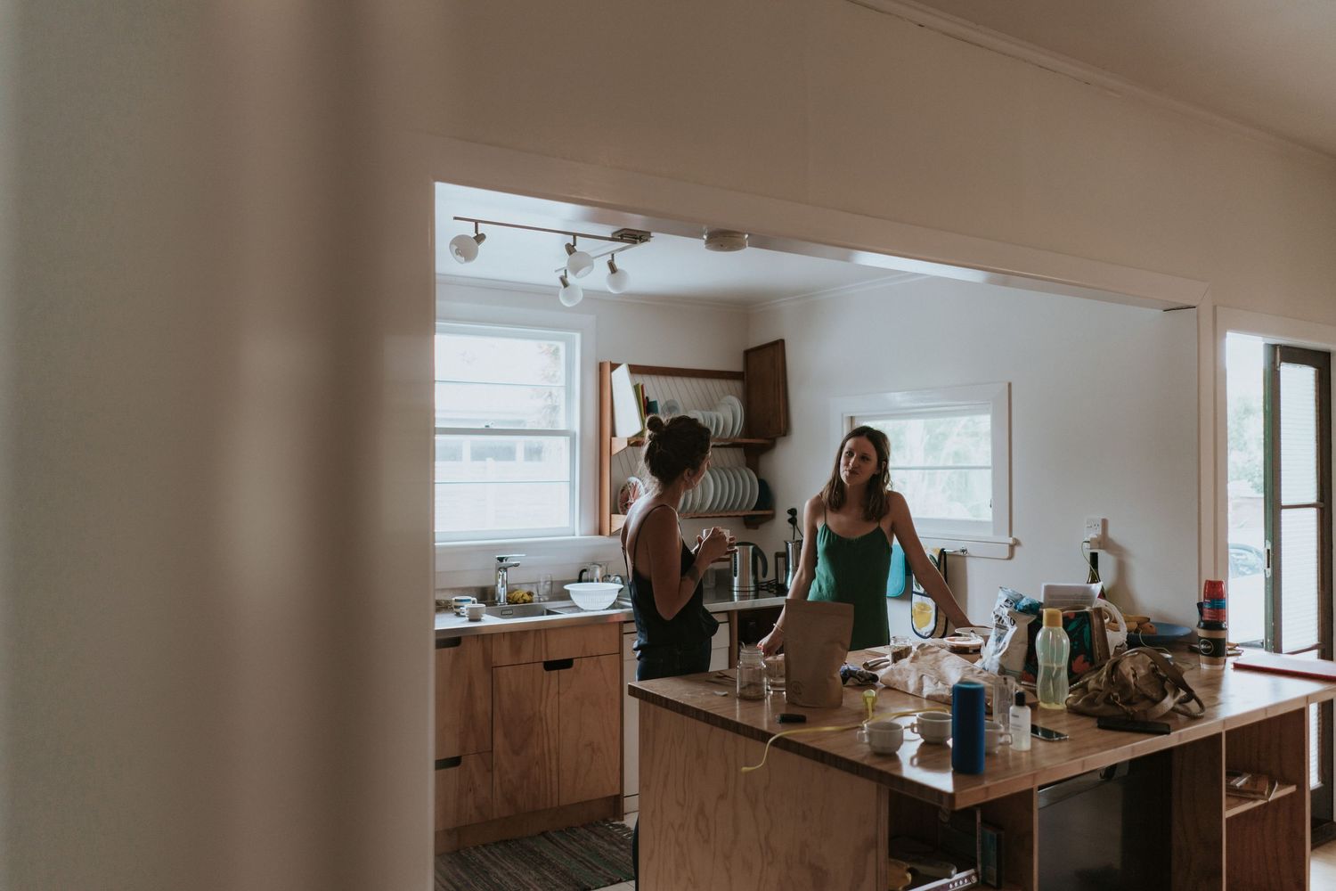 Two individuals preparing drinks and socializing in a modern kitchen with natural lighting.
