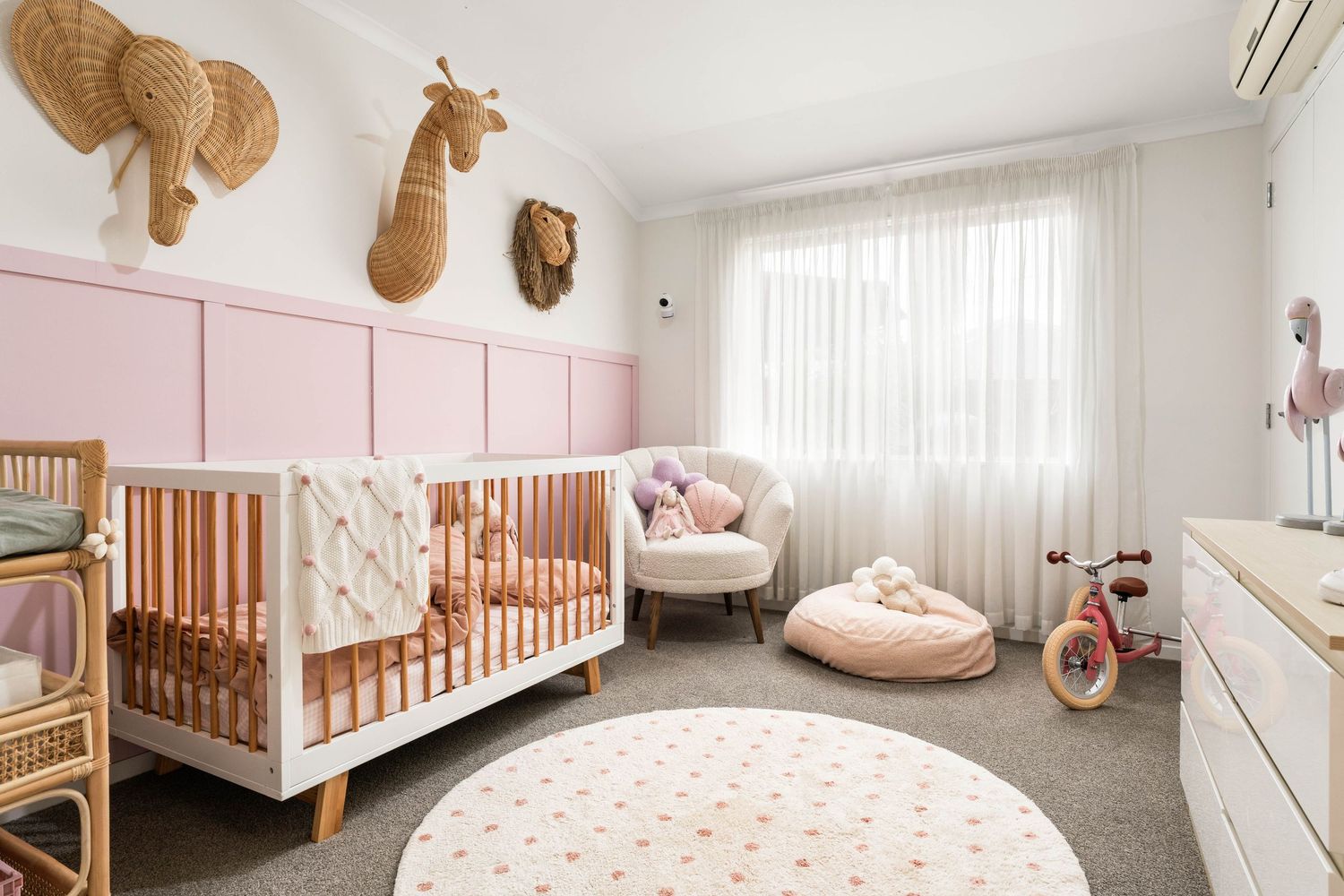 Panoramic view of a modern nursery featuring natural wood furniture, pink accents, and white walls.