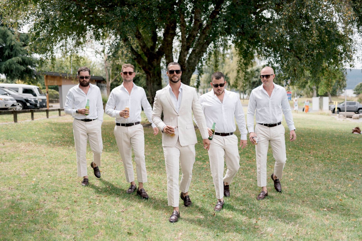 A group walks together on a grassy lawn wearing matching white outfits in a casual outdoor setting.