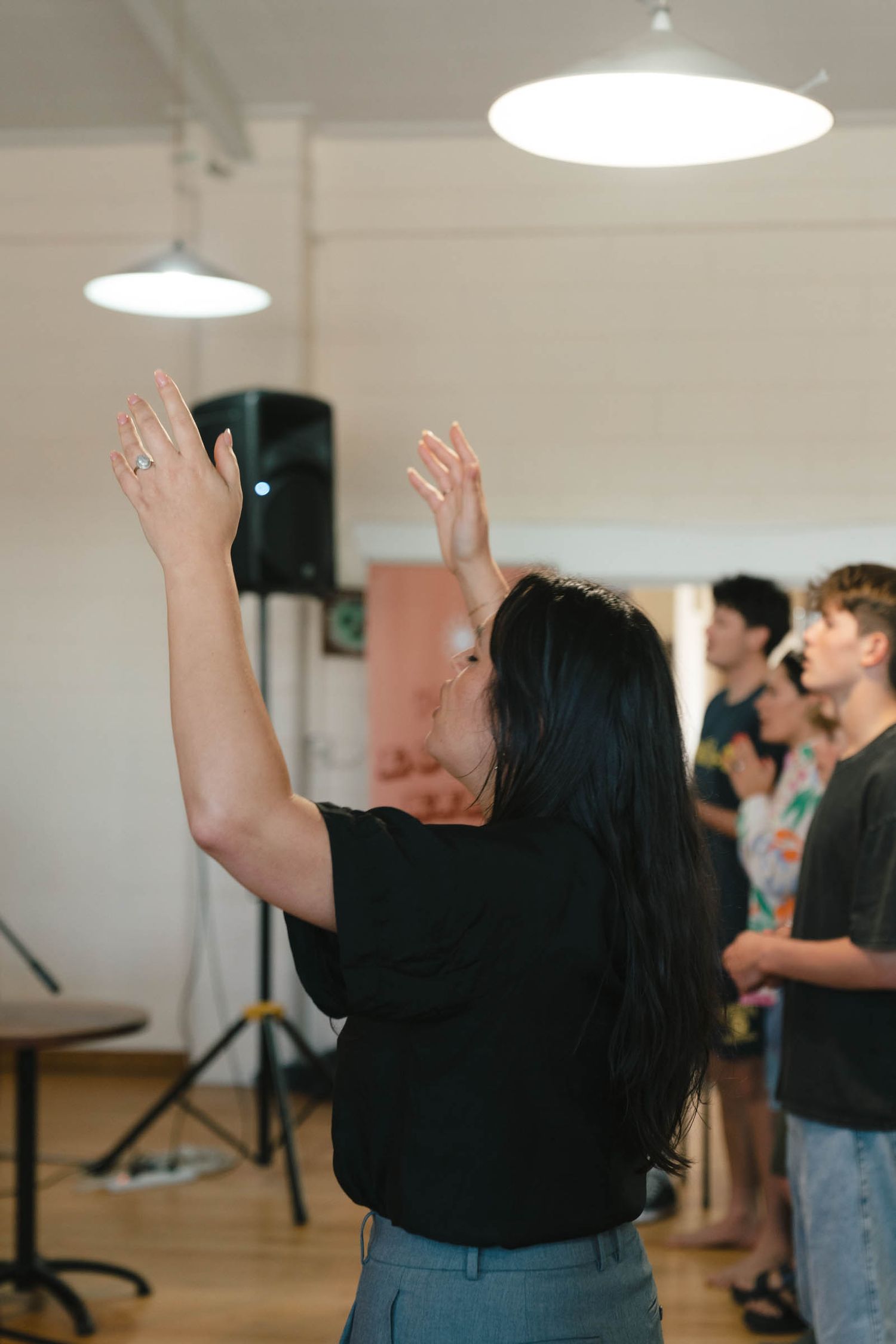 Person with raised arms during worship service in a bright indoor space.