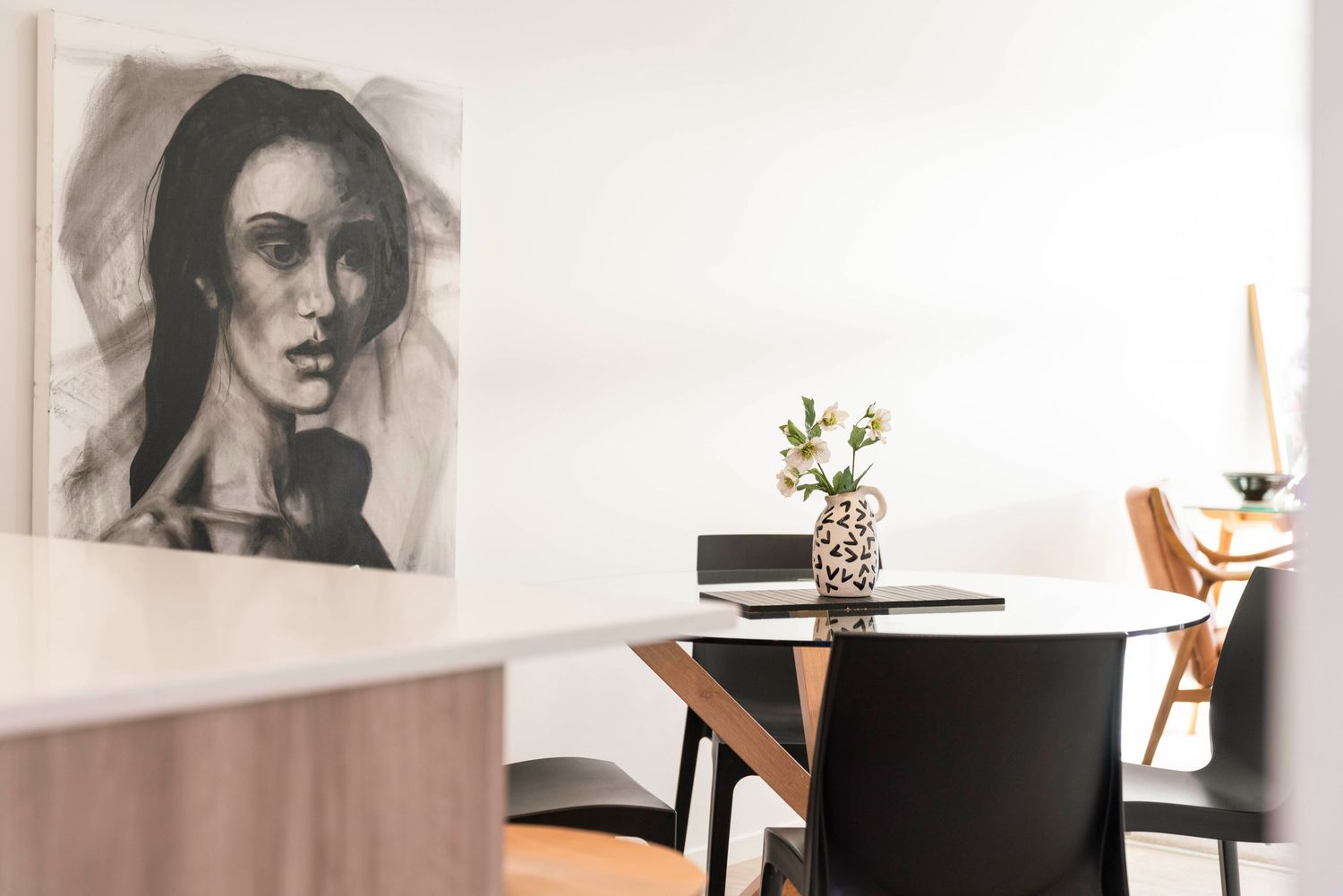 A minimalist dining area featuring a round white table, black chairs, and monochromatic artwork on the wall.
