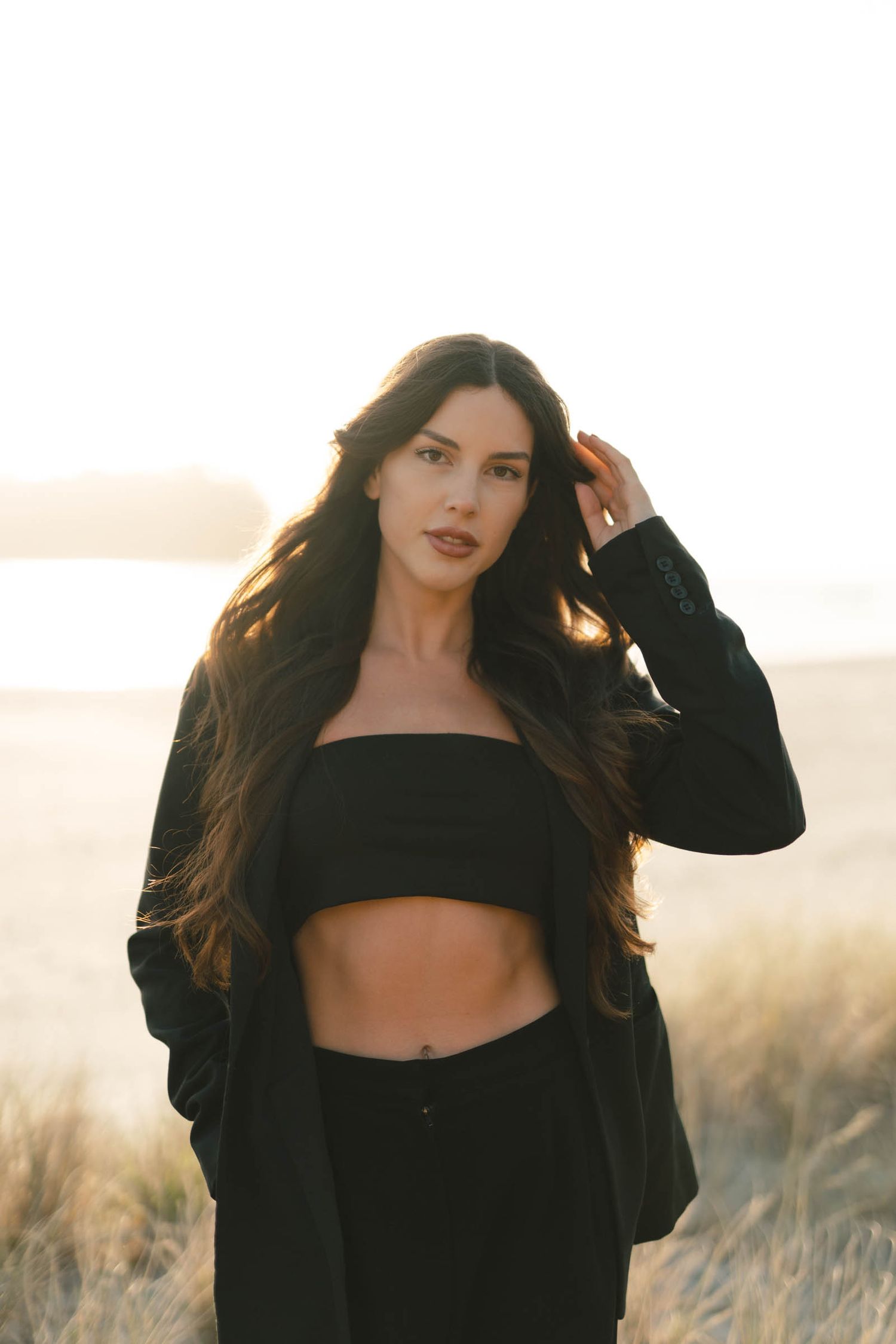 Stylish portrait in black ensemble against backdrop of sunset and wild grass.