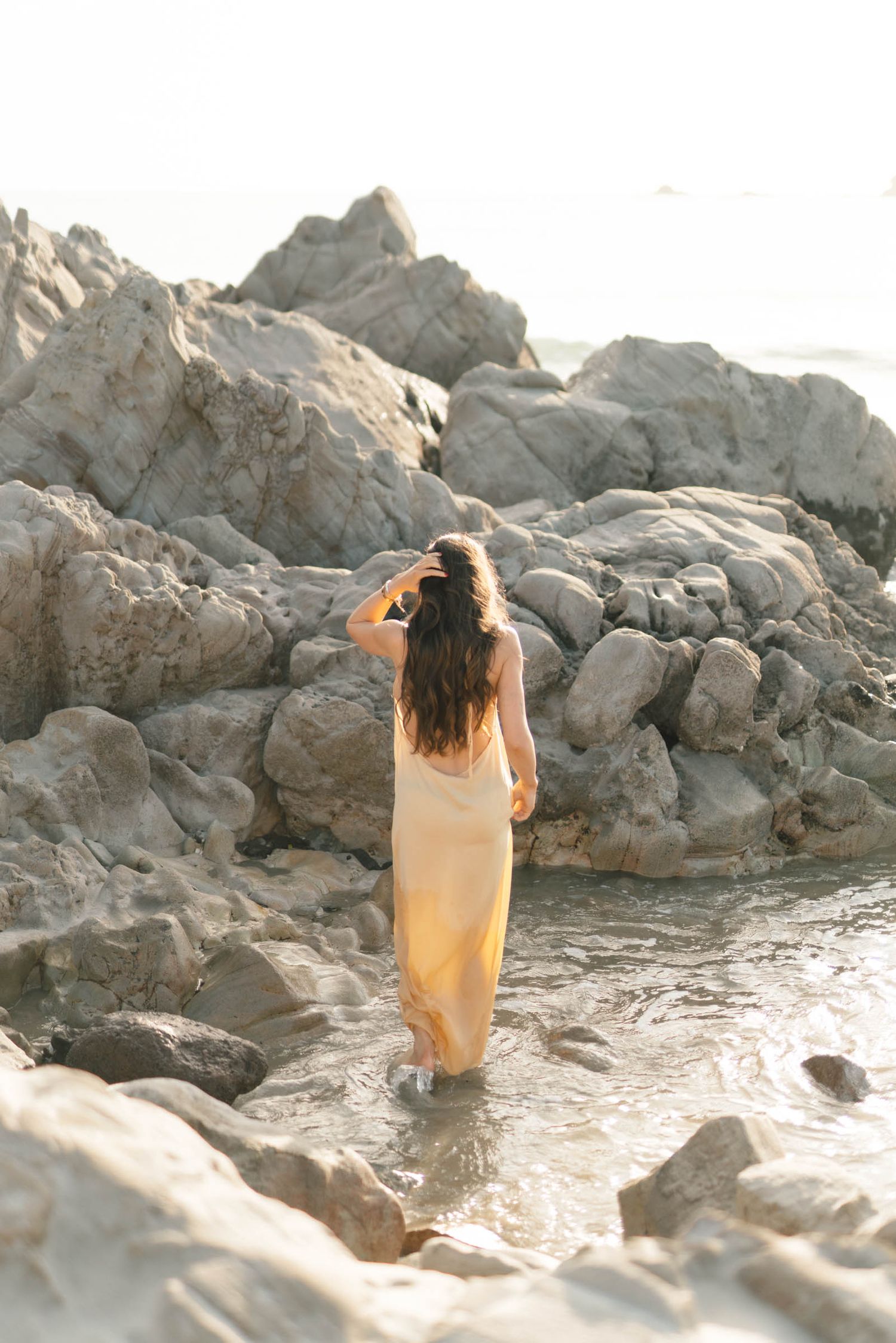 A dreamy photoshoot on rocky coastal terrain with soft golden light illuminating a flowing dress.