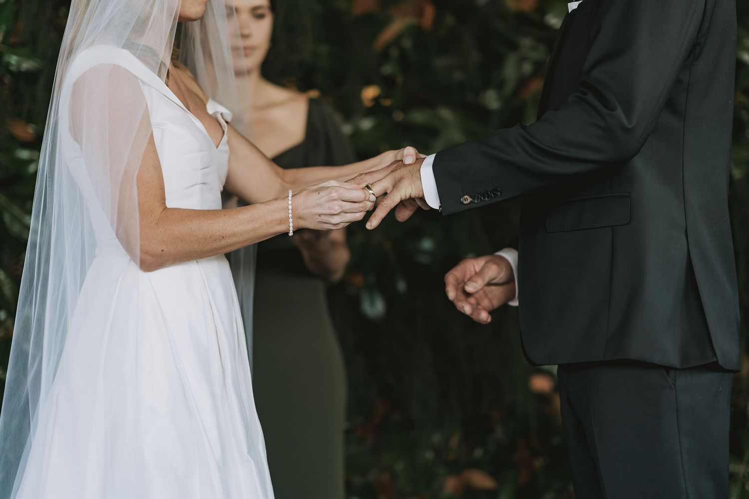 Close-up of bride and groom exchanging rings during wedding ceremony with white bridal veil.