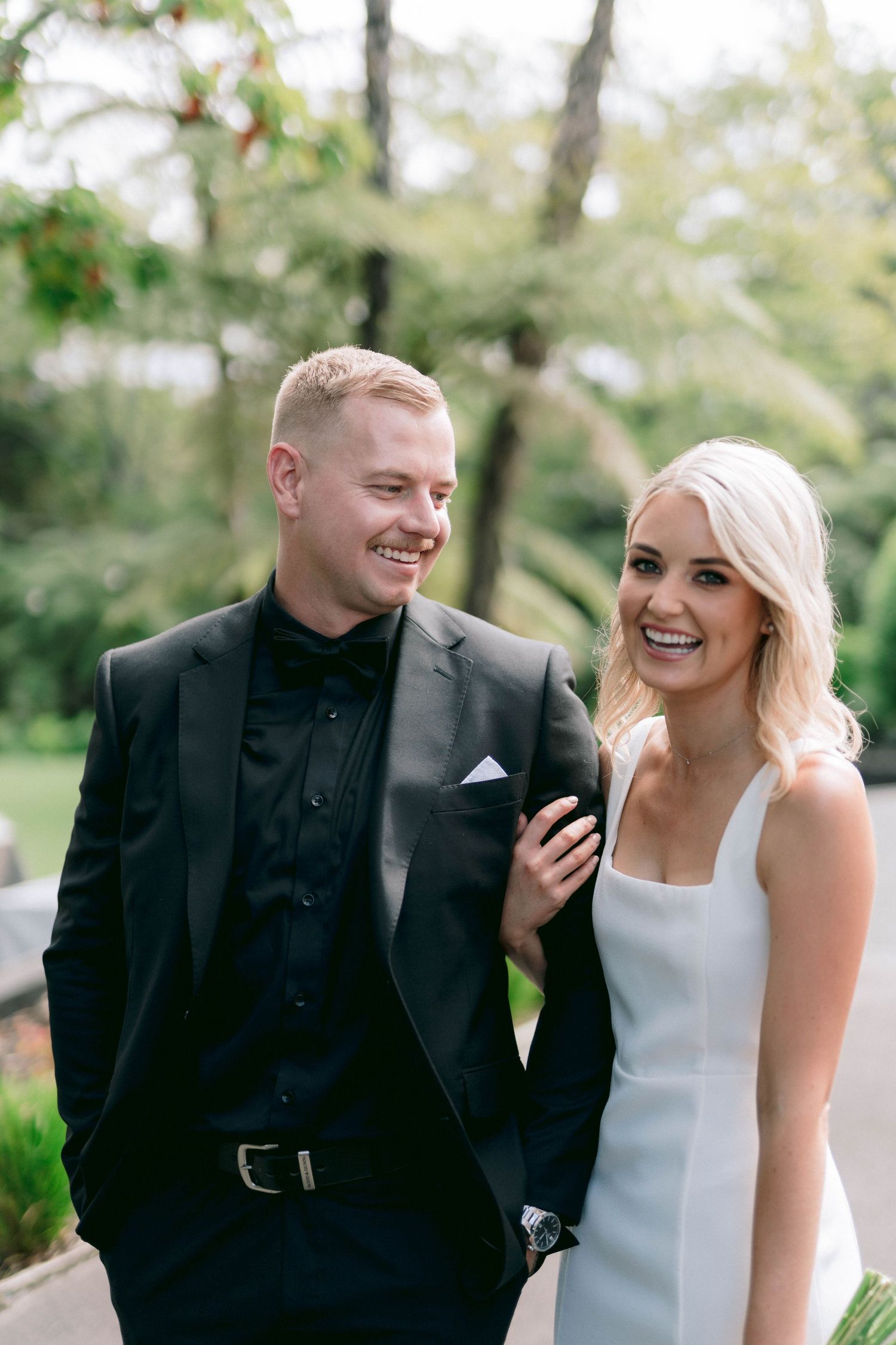 Happy couple shares a candid moment outdoors during their wedding day wearing classic black and white attire.