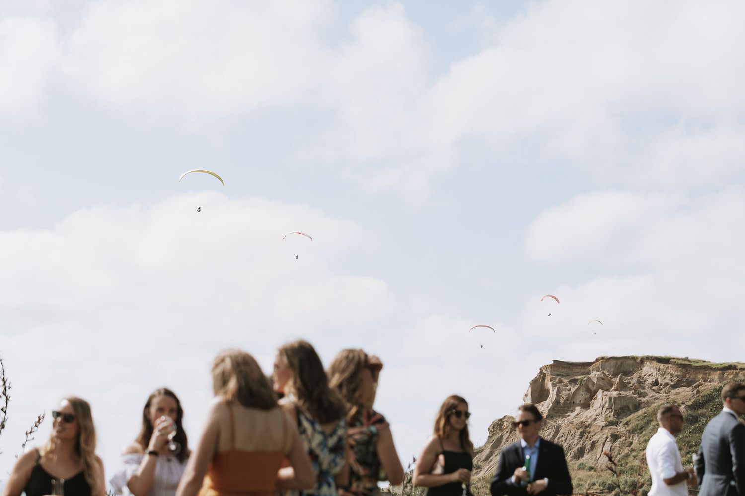 Silhouettes of wedding guests seated in multiple rows against a warm sunset sky at an outdoor ceremony.