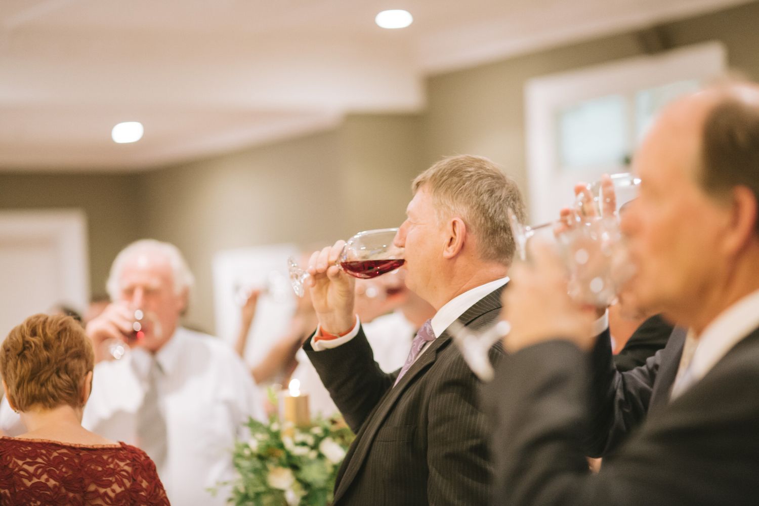 Group of guests drinking wine at an elegant indoor celebration event with recessed lighting.