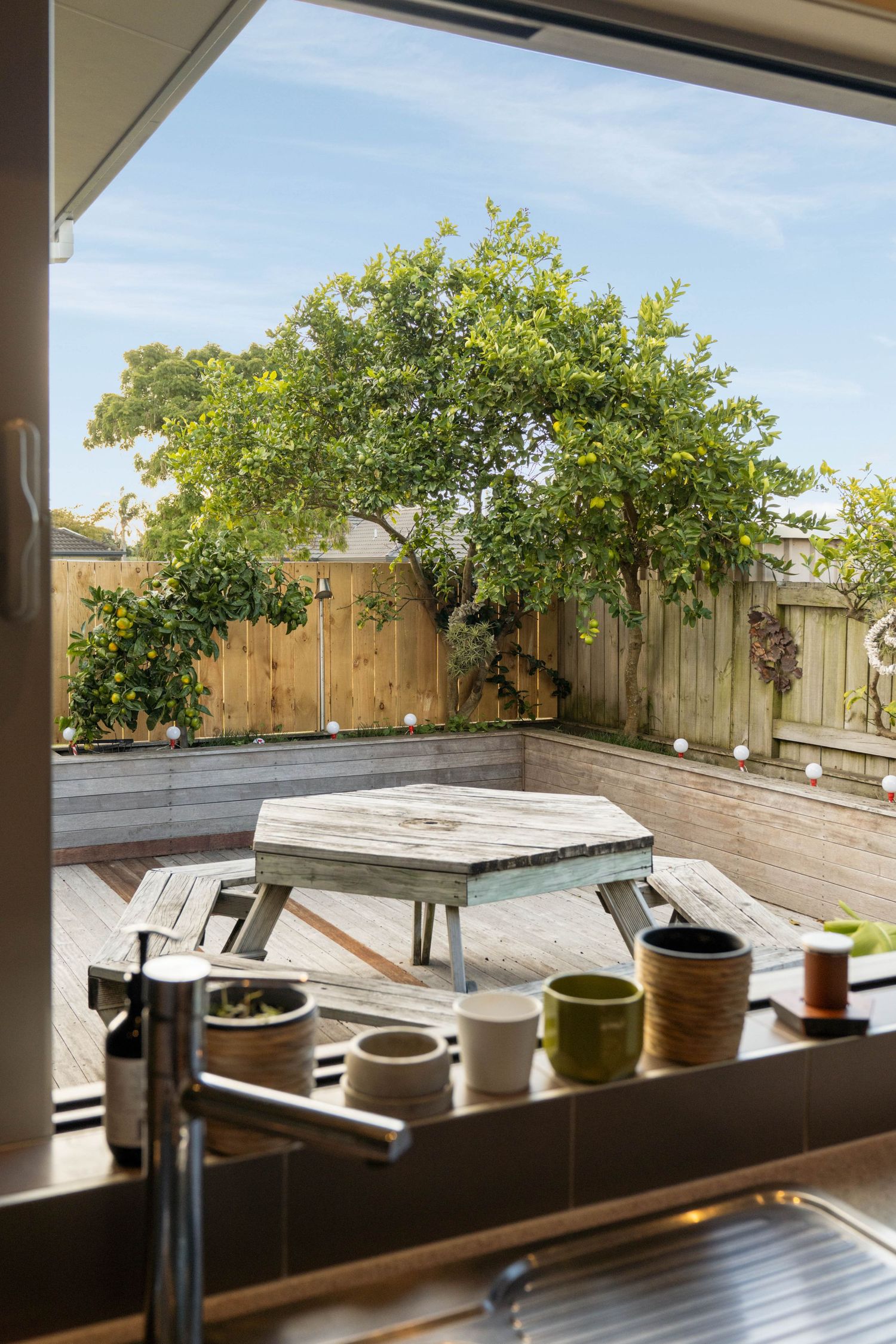 Panoramic view of a modern deck with a built-in hot tub surrounded by potted plants and wooden fencing in a backyard.