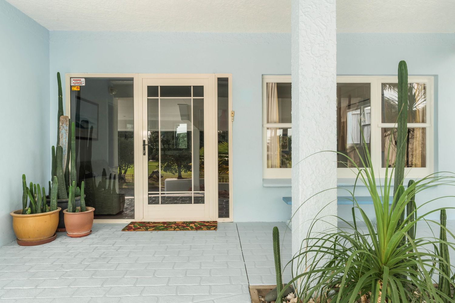 Modern home entrance with light blue walls, white columns, and potted cacti decorating the front porch.