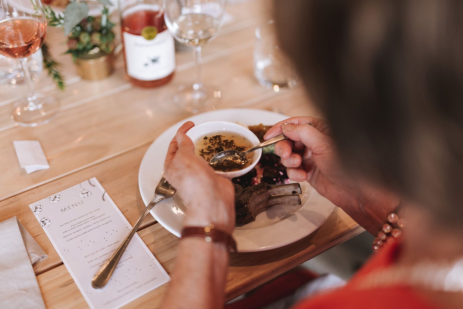Someone cuts into a dish at a restaurant table with a menu and wine glasses visible in the background.