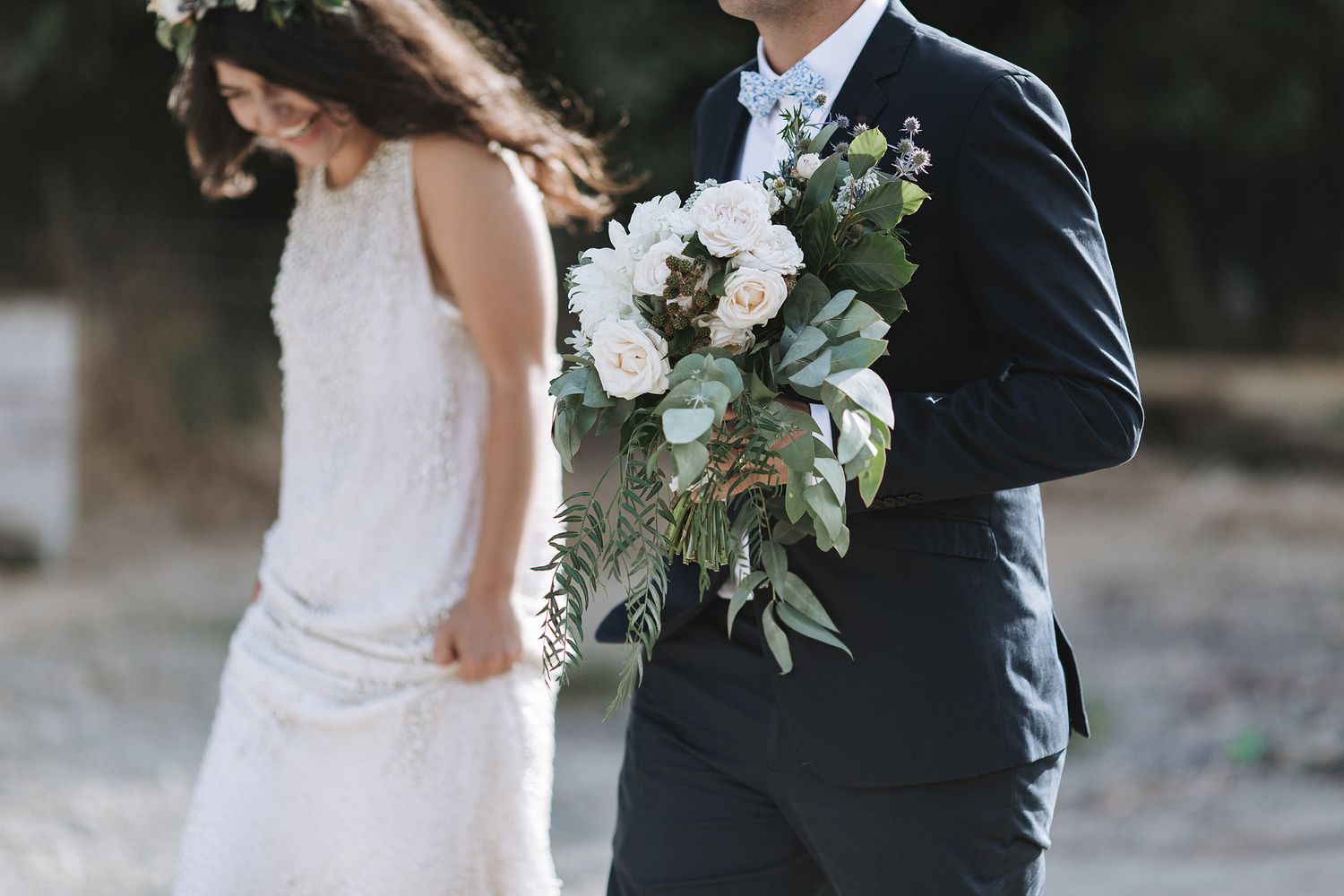 A newlywed couple stands close together with a beautiful white and green wedding bouquet against a blurred natural background.