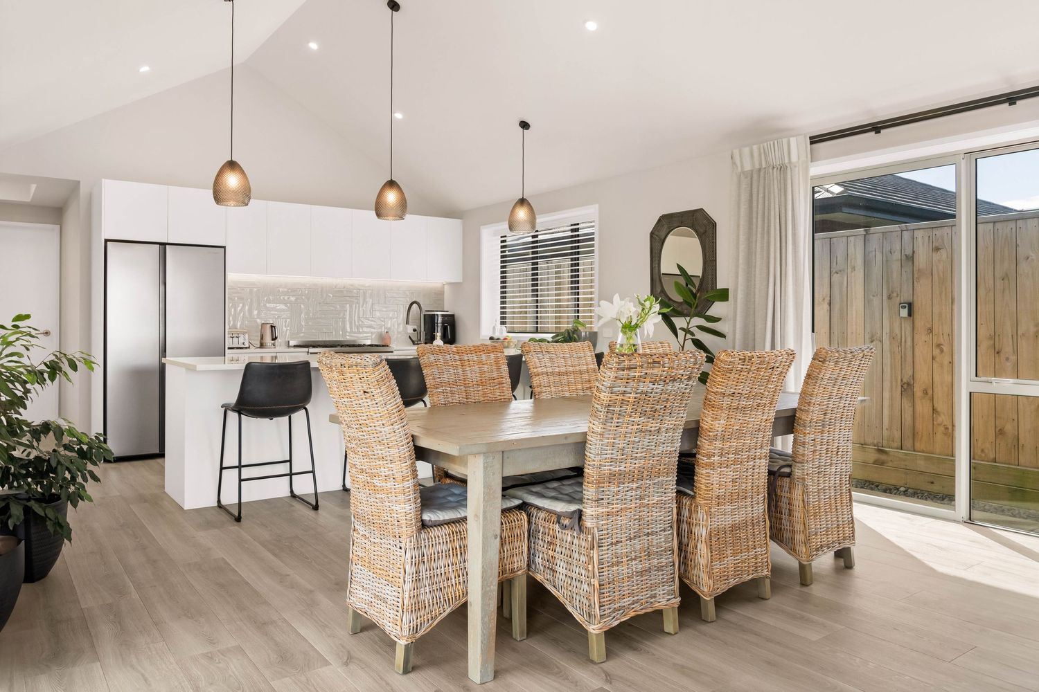 Contemporary dining room featuring rattan chairs and pendant lighting with natural light streaming through windows.