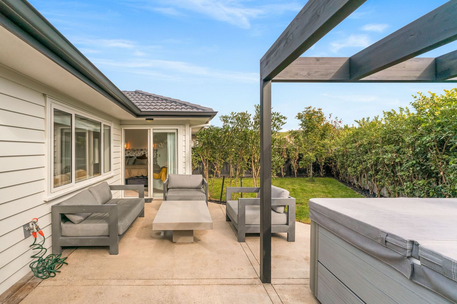 Contemporary covered patio with outdoor furniture and cream-colored siding on the house exterior.