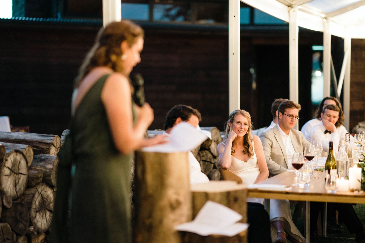 Wedding reception guests listen to speeches during outdoor evening celebration.
