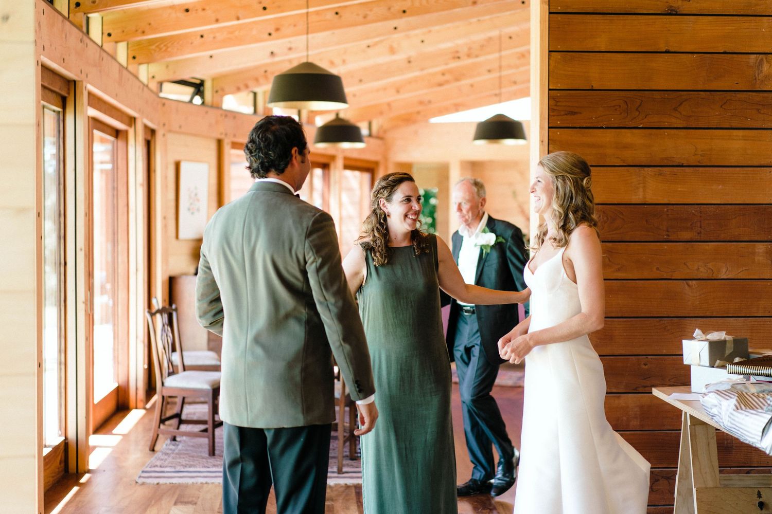 People gathered inside rustic wooden cabin with large windows and pendant lights.