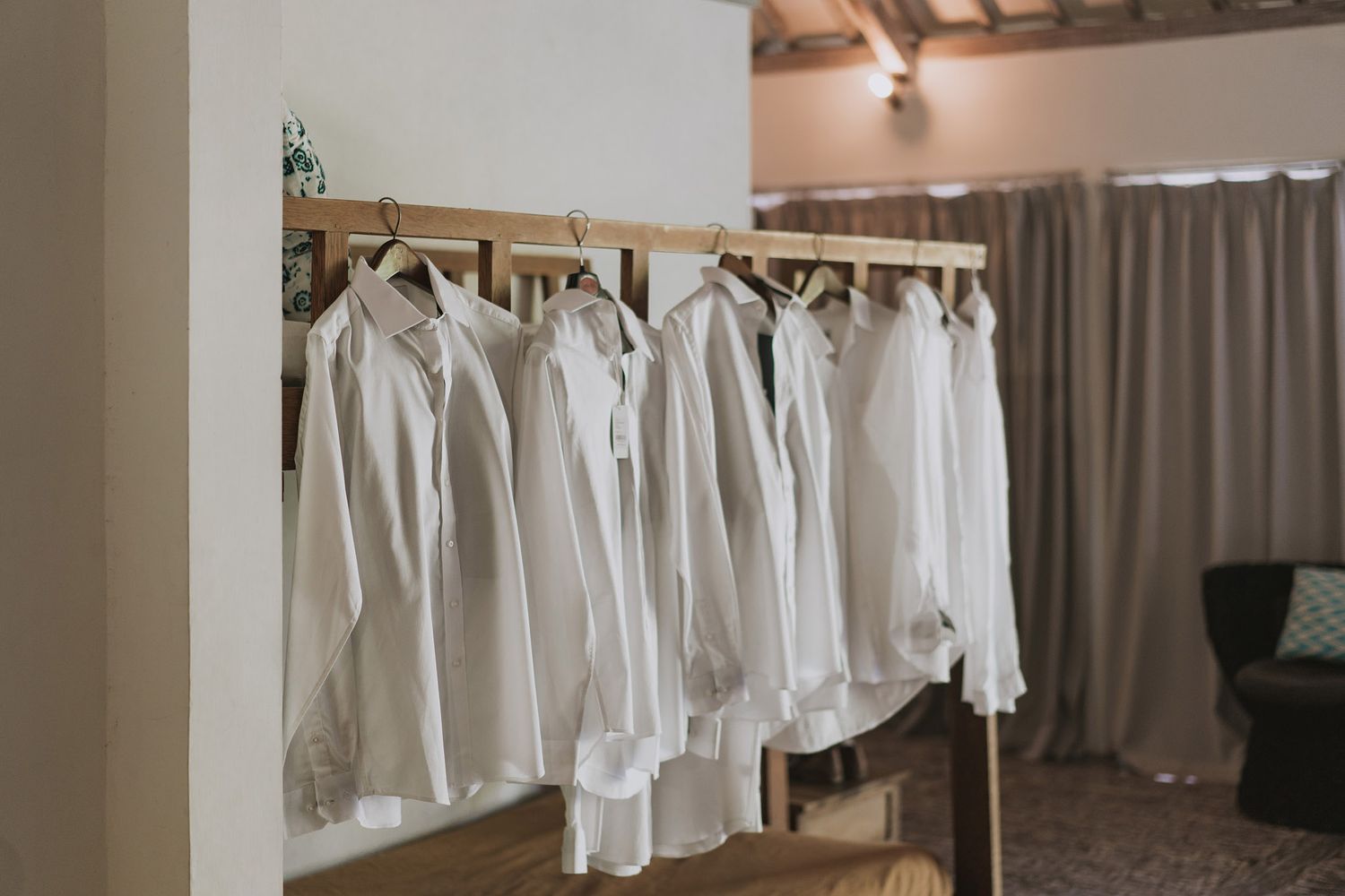 Row of white dress shirts hanging neatly on wooden hangers against a light colored wall.