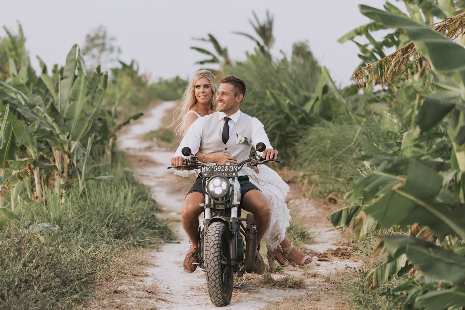 Couple enjoying a romantic motorcycle ride through lush tropical vegetation.