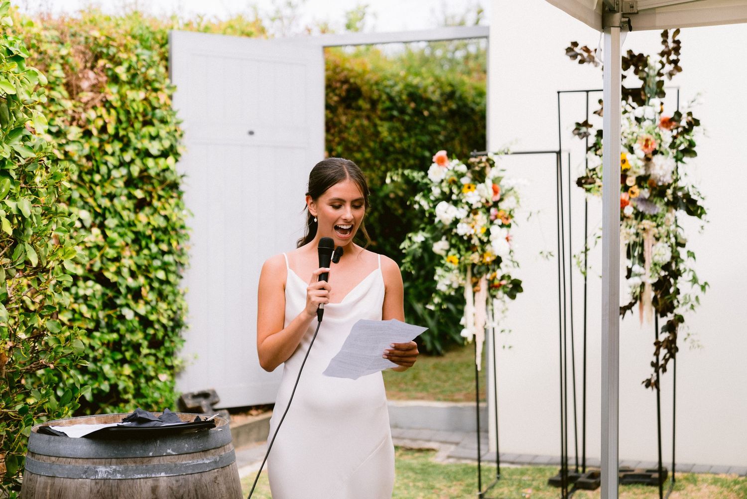 Elegant wedding party members posing in front of garden greenery and white architecture.
