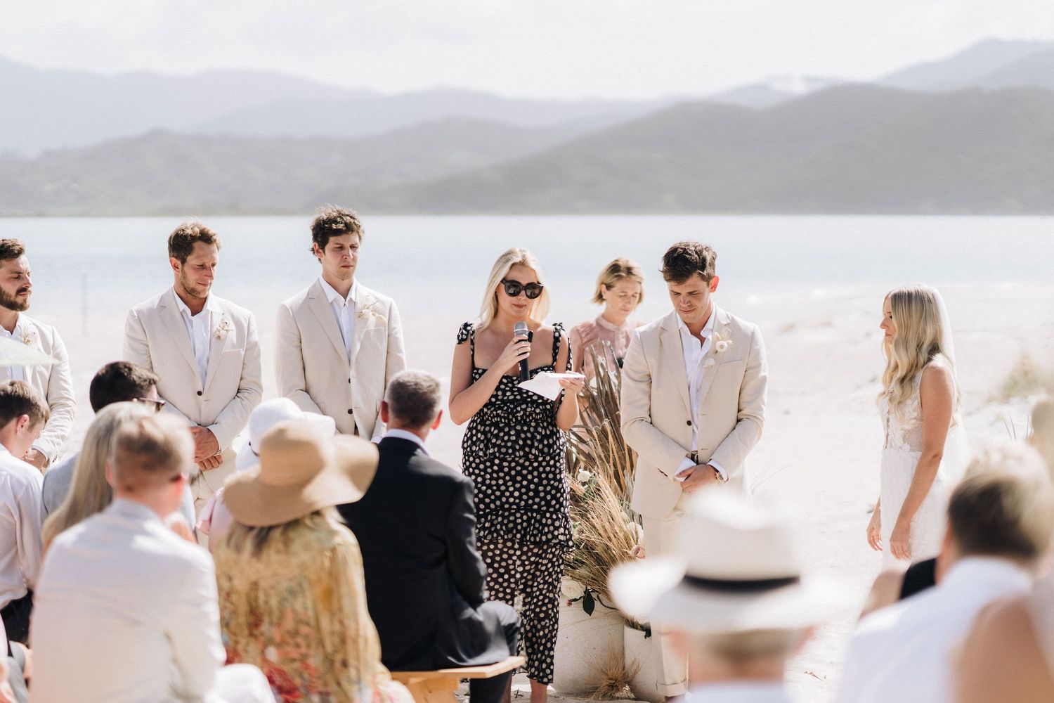 Beachfront wedding celebration with guests in light summer attire overlooking a scenic bay.
