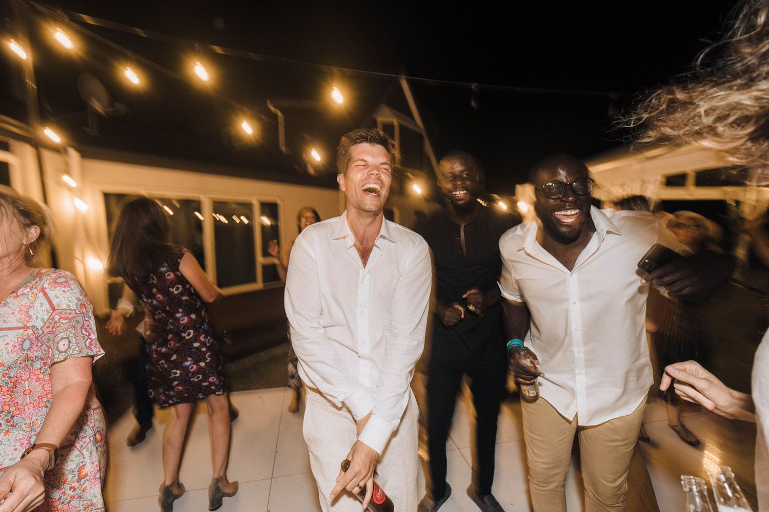 Wedding celebration under string lights with guests dancing and enjoying the nighttime festivities.