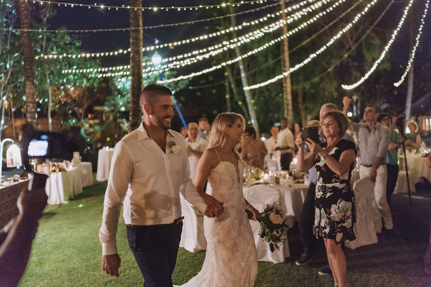 Guests celebrate under string lights at an outdoor evening wedding reception.