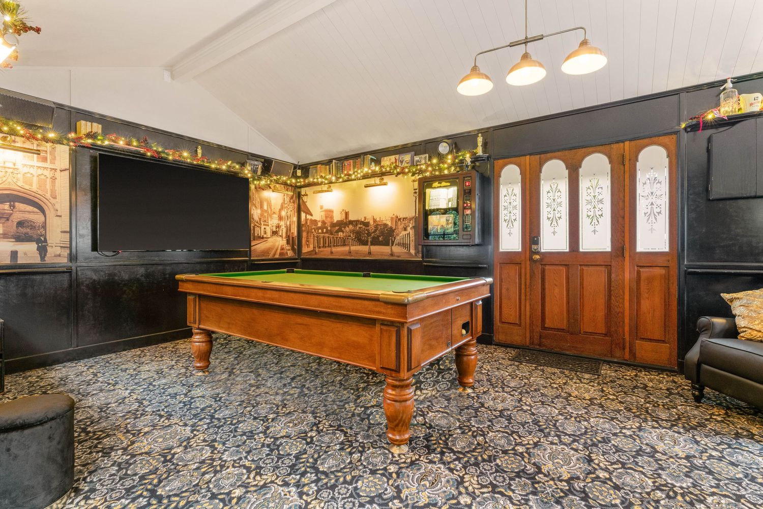 Game room with vintage pool table, dark walls adorned with murals, and ornate wooden doors.
