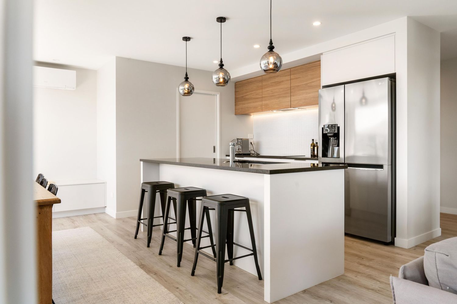 Modern open concept apartment with warm wood floors, black pendant lights, white walls and sleek kitchen design.