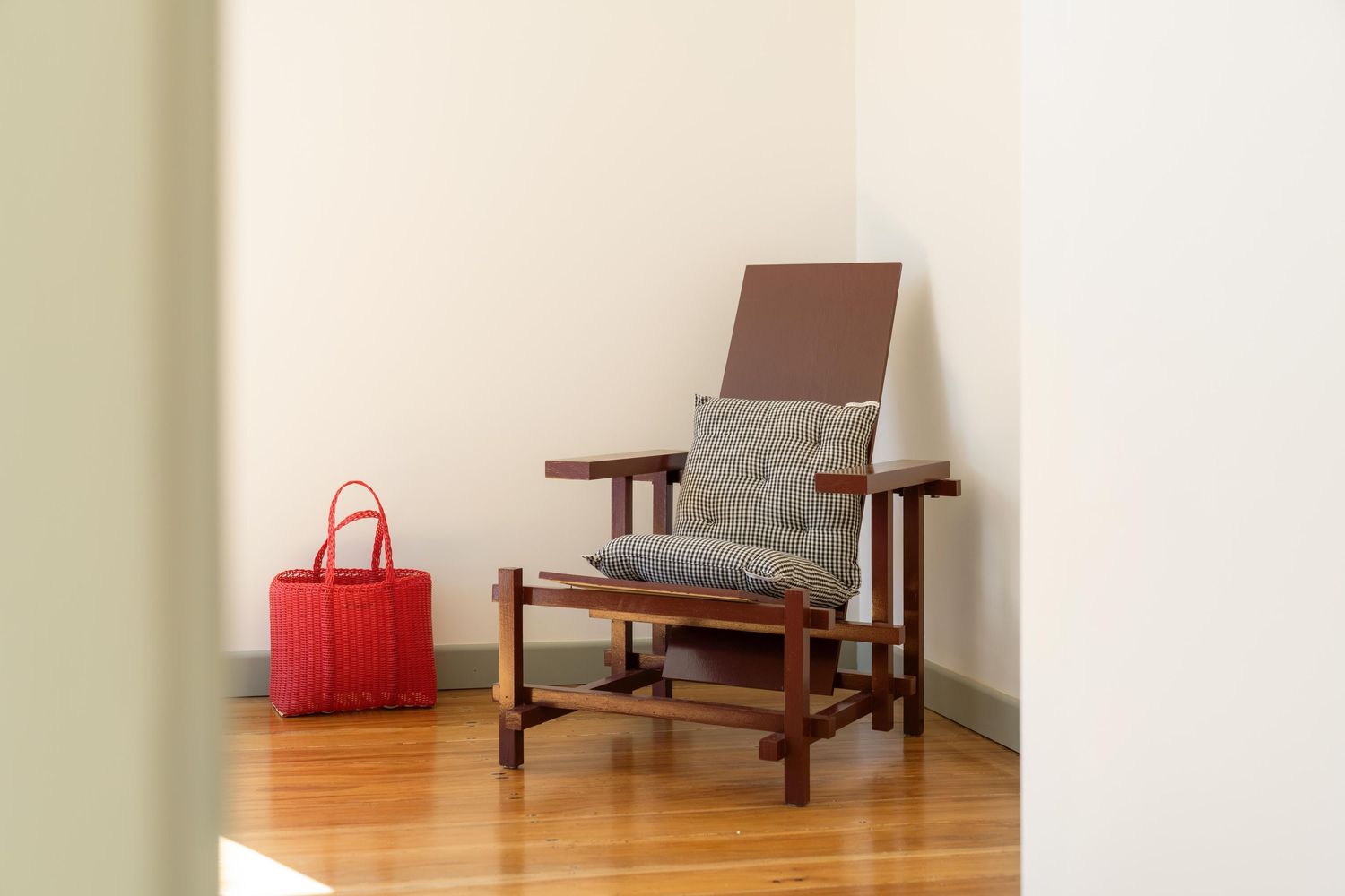 Wooden armchair with grey cushions and red handbag on hardwood flooring.