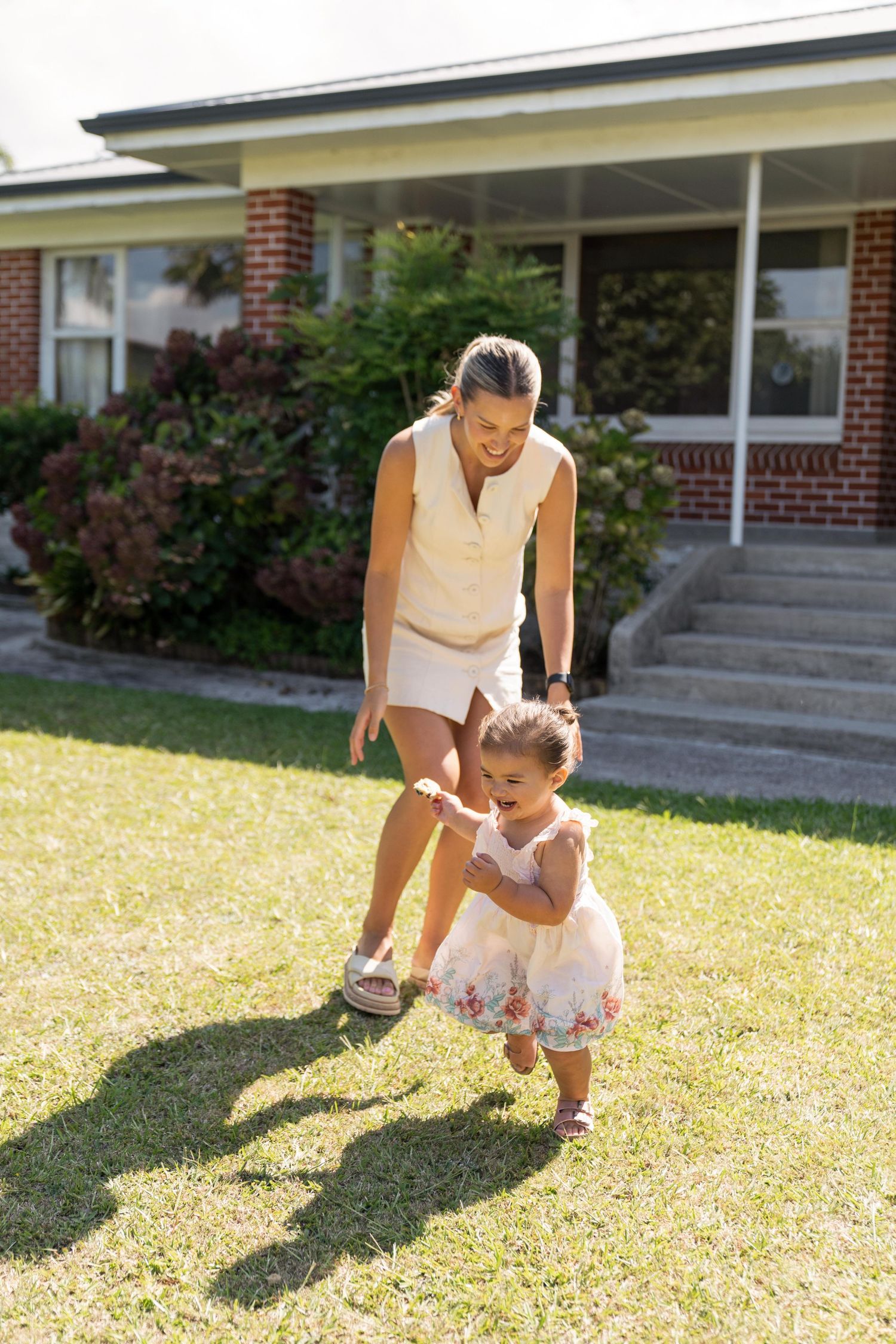 People playing together on a sunny lawn in front of a brick house.
