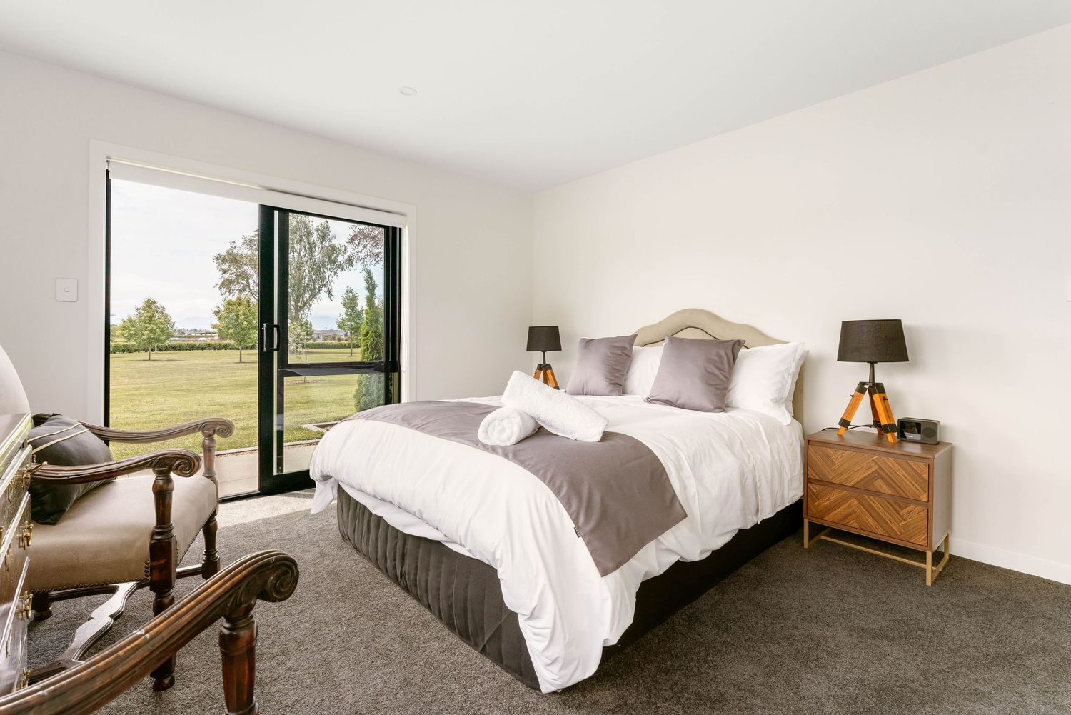 Contemporary bedroom with large window offering countryside views, featuring grey and white bedding.