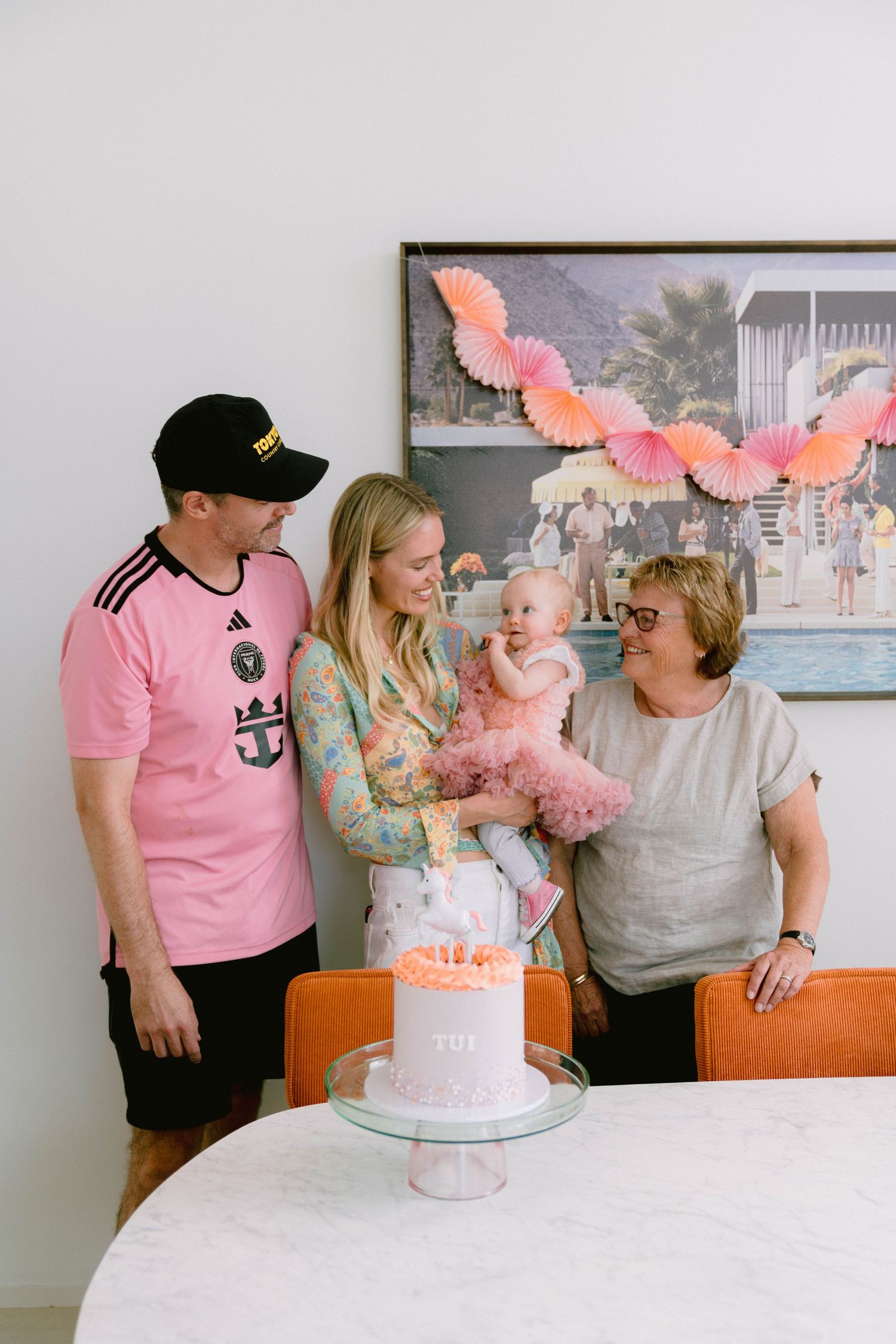 Family gathered around a pink birthday cake with butterfly decorations on top celebrating a special occasion.