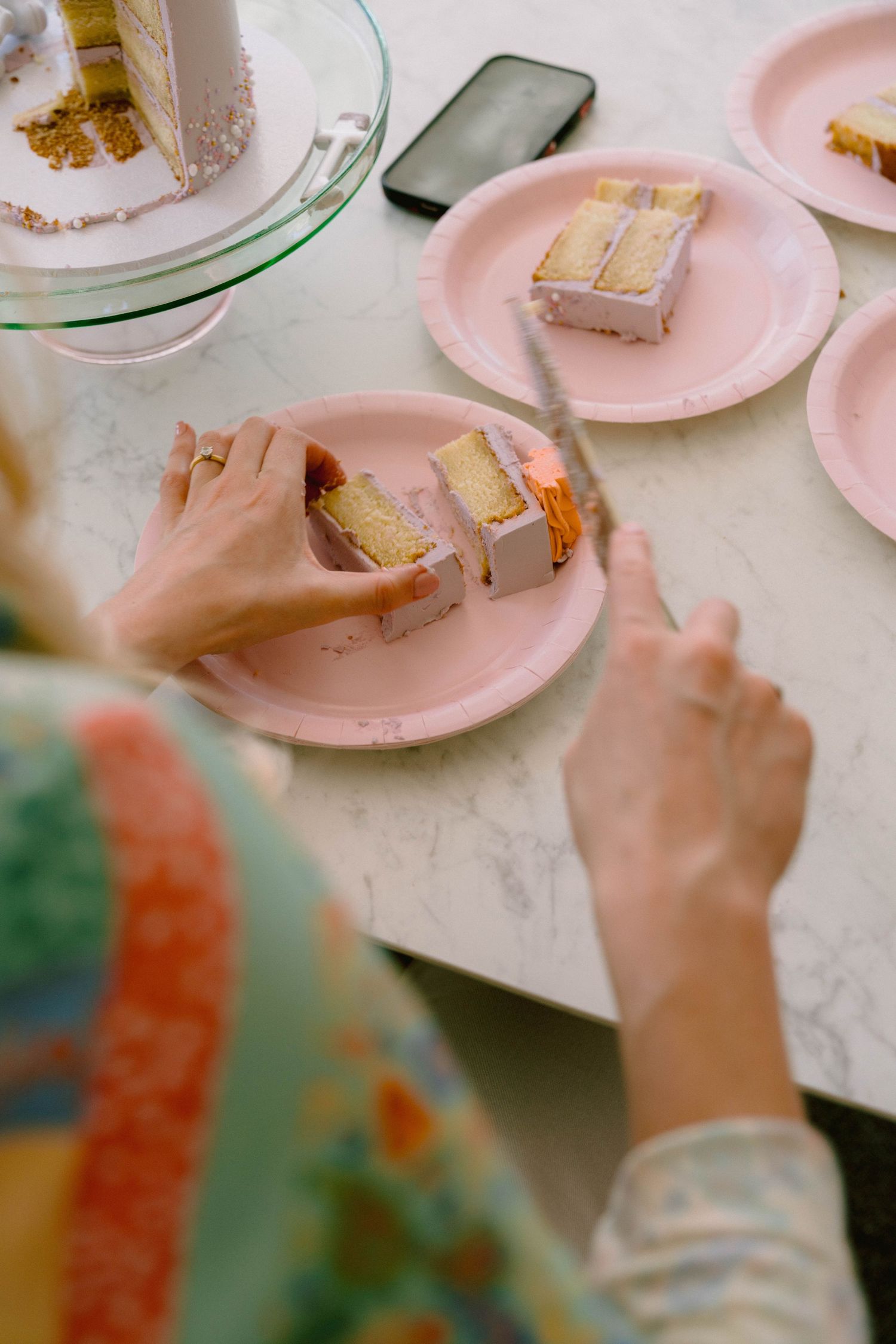 Pink plates with slices of cake and a smartphone on a white table at a party.
