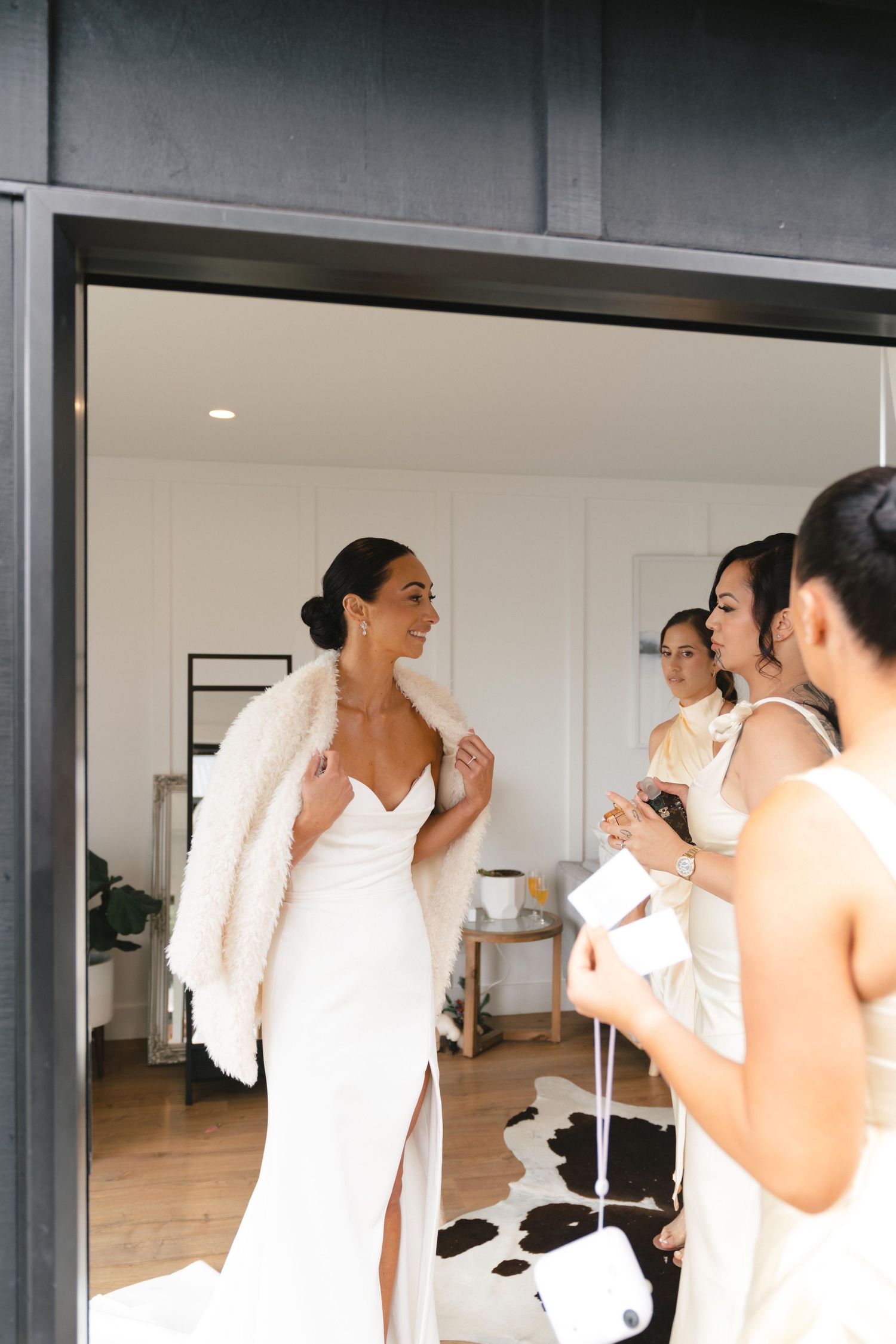 A bride in an elegant white dress with a fur wrap shares a joyful moment with her wedding party.
