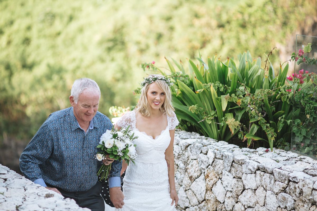 Outdoor garden wedding celebration with stone wall and tropical greenery backdrop.
