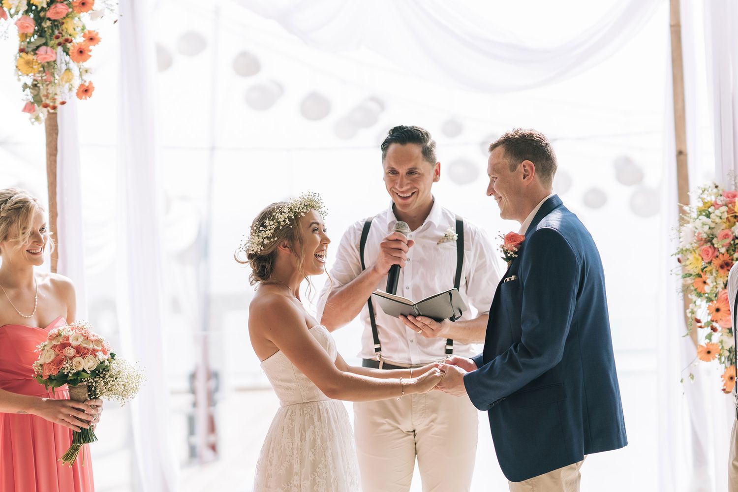 Beachside wedding ceremony with floral arch decorations in coral and white.