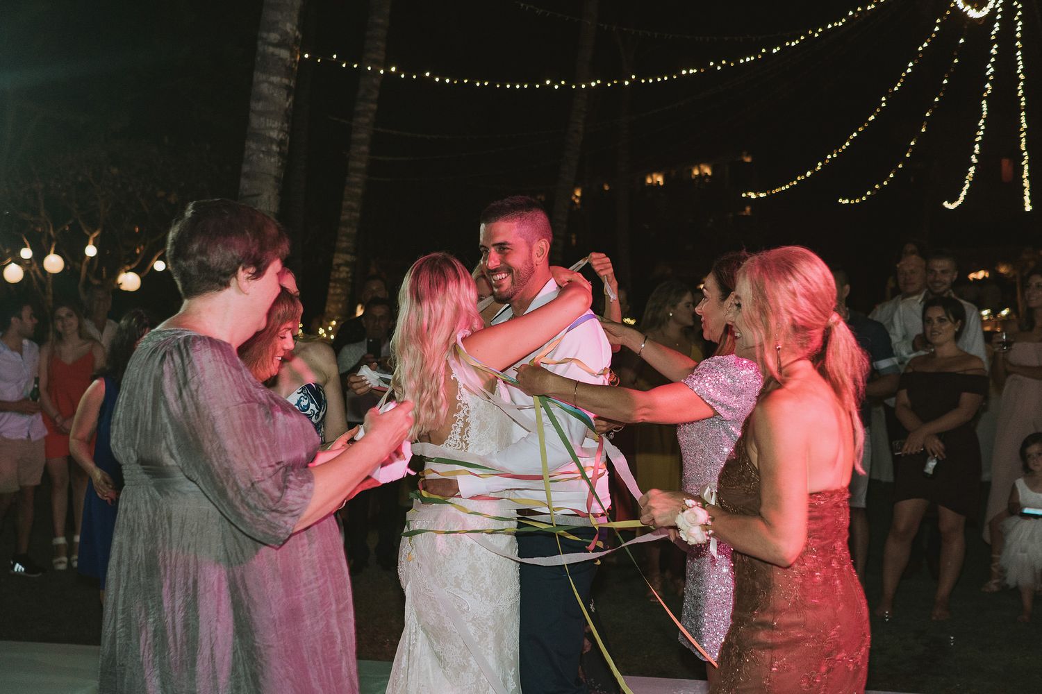 Wedding guests dancing together under string lights at an outdoor evening reception celebration.