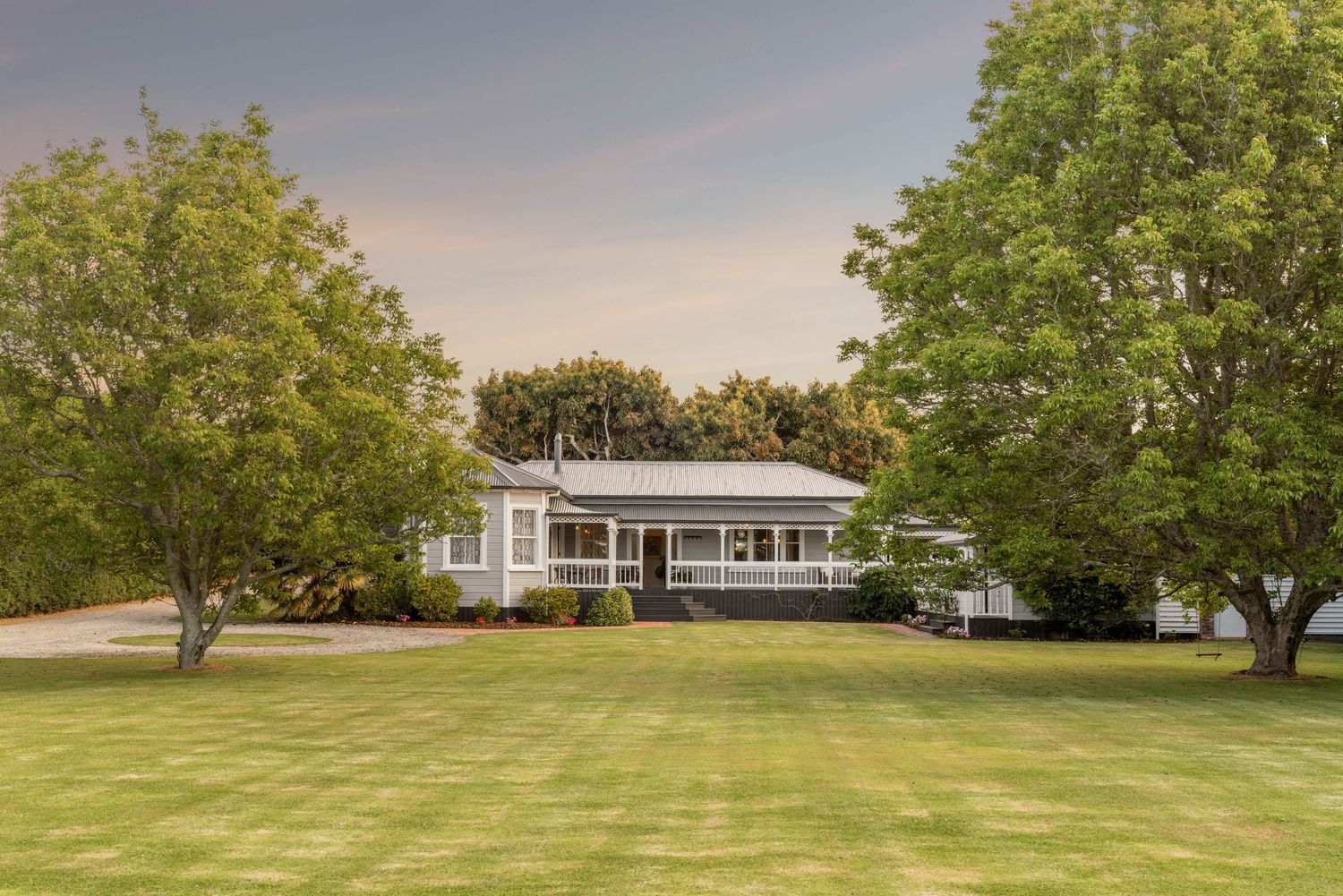 A panoramic view of a spacious rural property with a single-story ranch home surrounded by green lawn and mature trees.