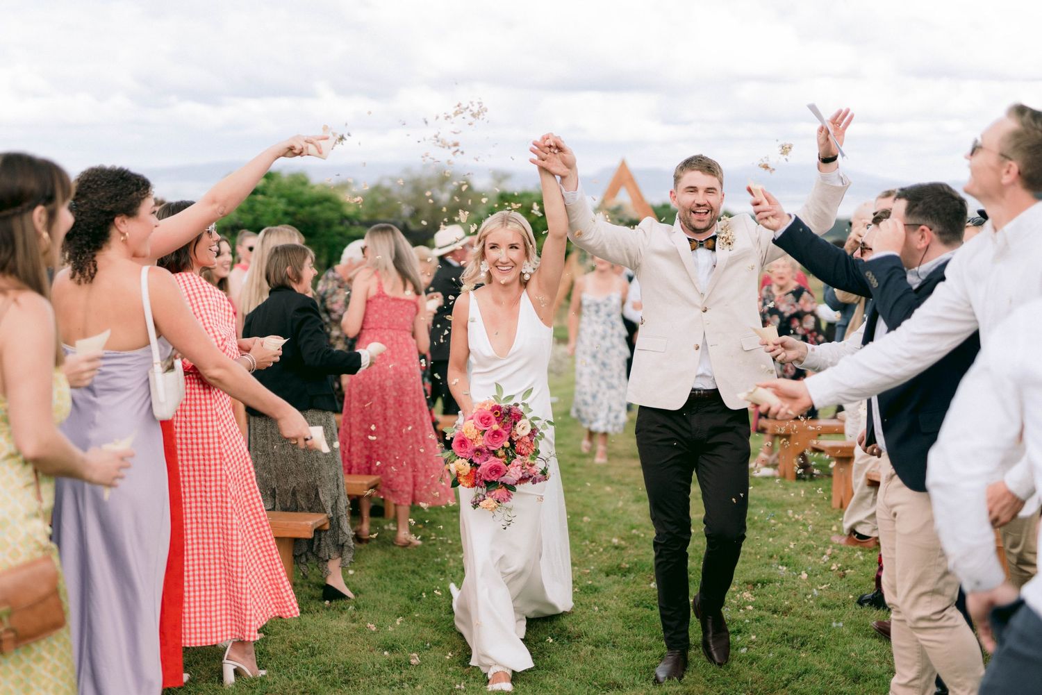 Wedding guests shower the newlyweds with confetti as they walk through a celebratory corridor.