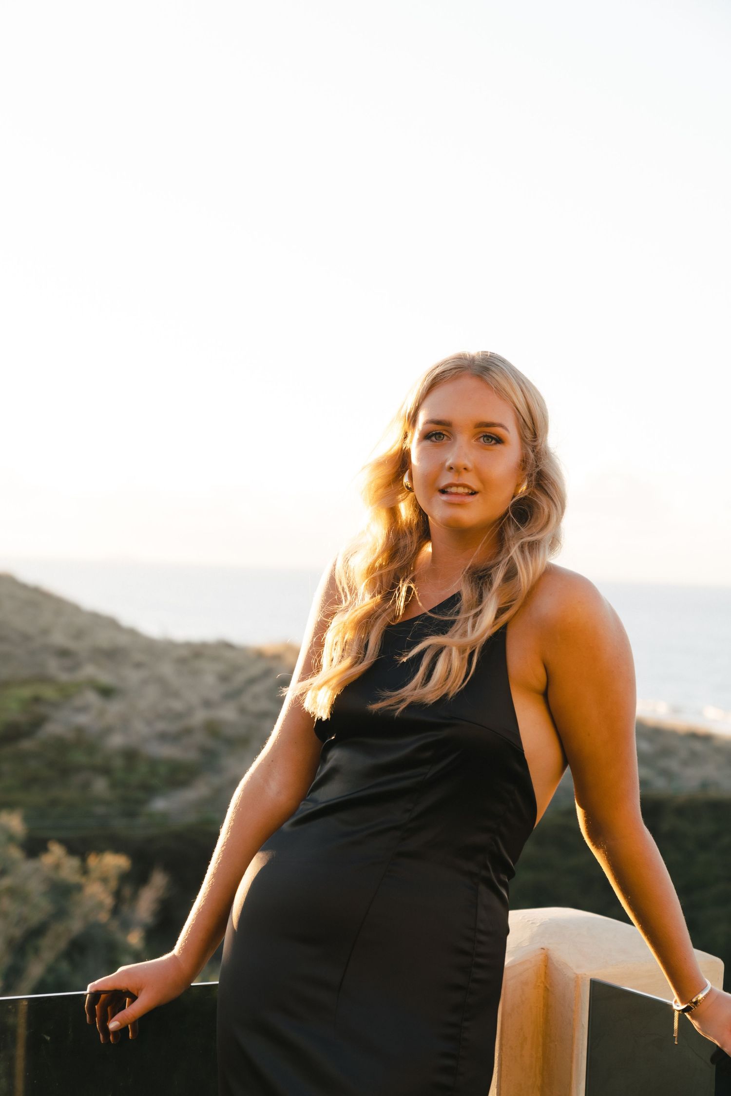 Woman in black dress smiling on outdoor balcony during golden hour.