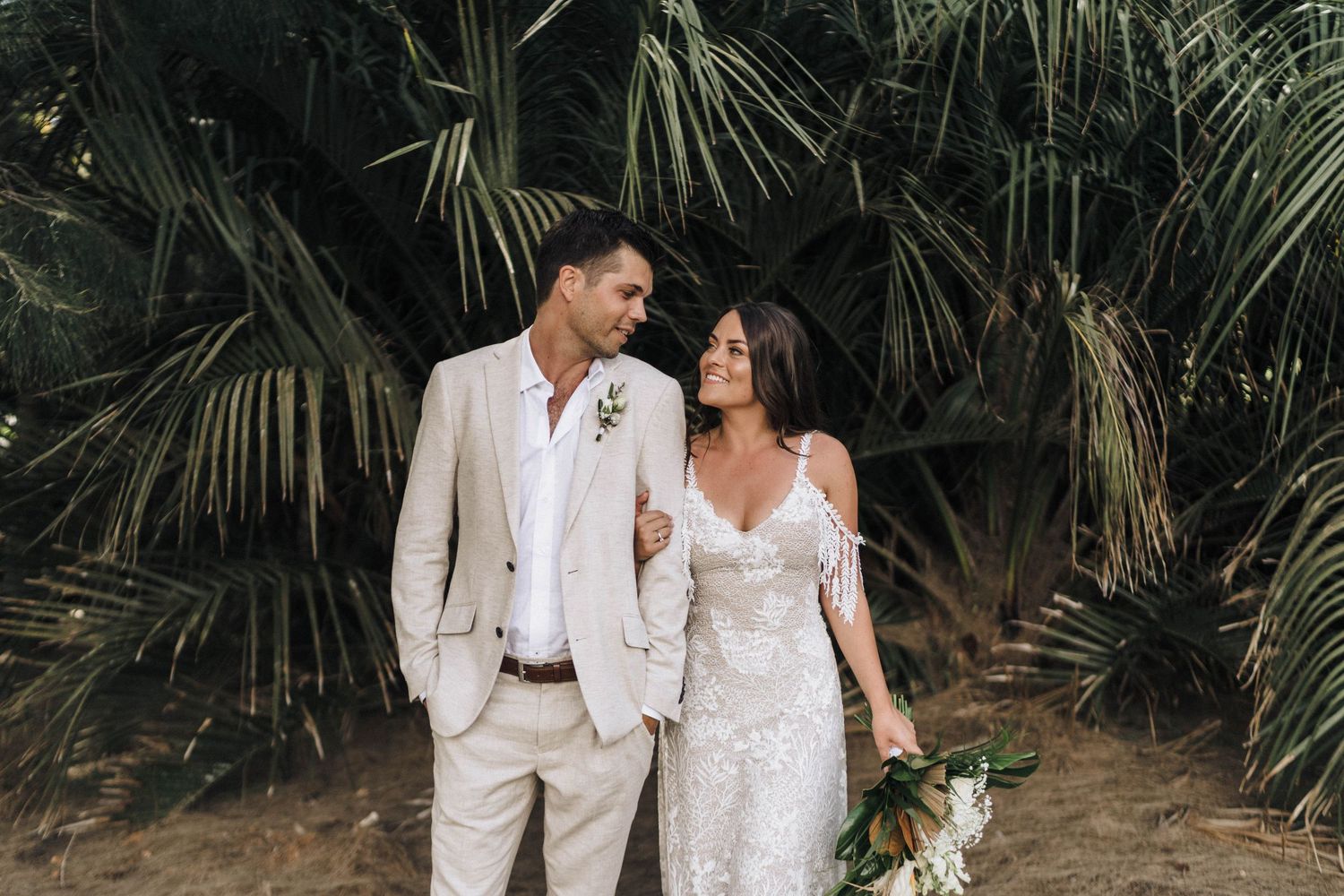 A romantic wedding couple shares an intimate moment among tropical palm fronds.