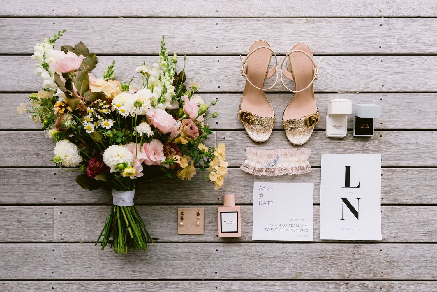 Wedding accessories including bouquet, shoes, and invitations arranged on rustic wooden planks.