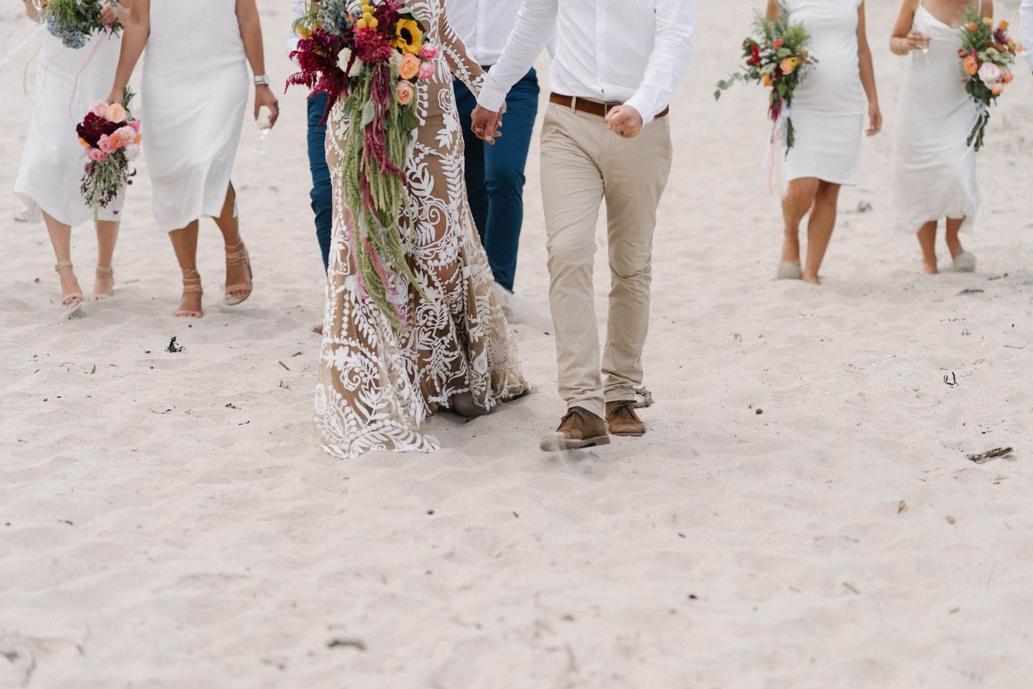 Barefoot group in white and beige clothing walking on a sandy beach during golden hour lighting period.