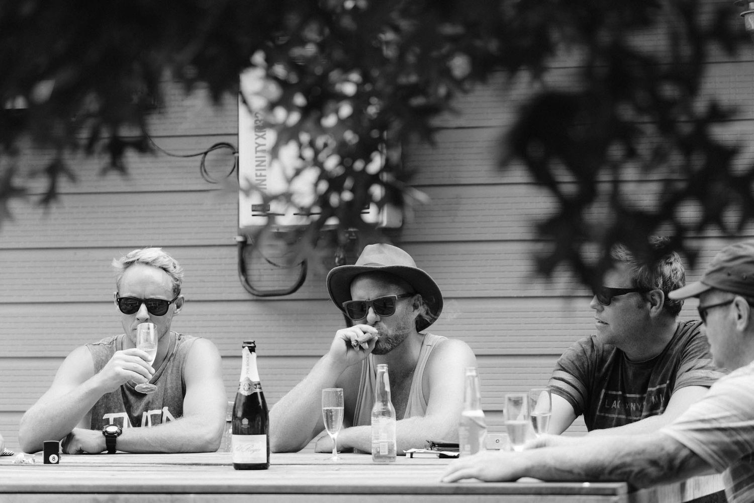 People wearing sunglasses and casual attire enjoy drinks at an outdoor table in monochrome style.