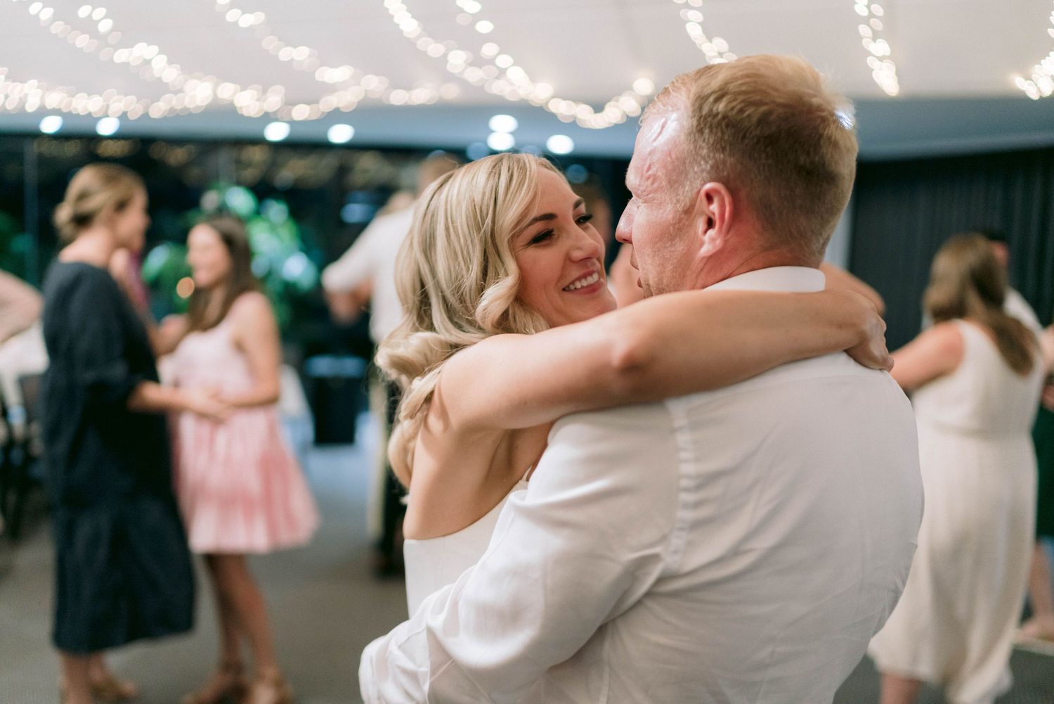 A romantic moment on the dance floor under twinkling lights at an evening wedding reception.